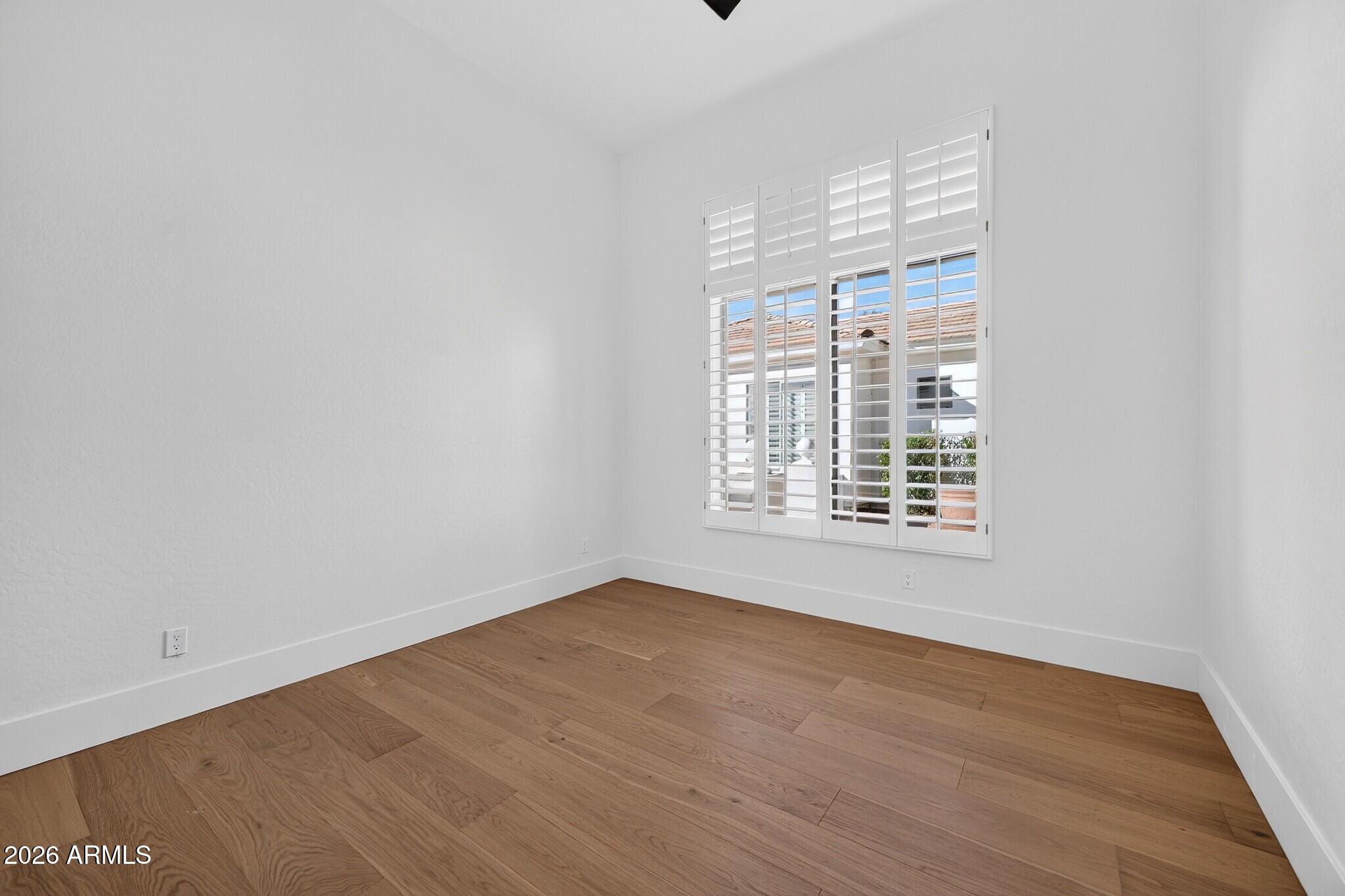 Empty room with wood floors and a large plantation-shuttered window.