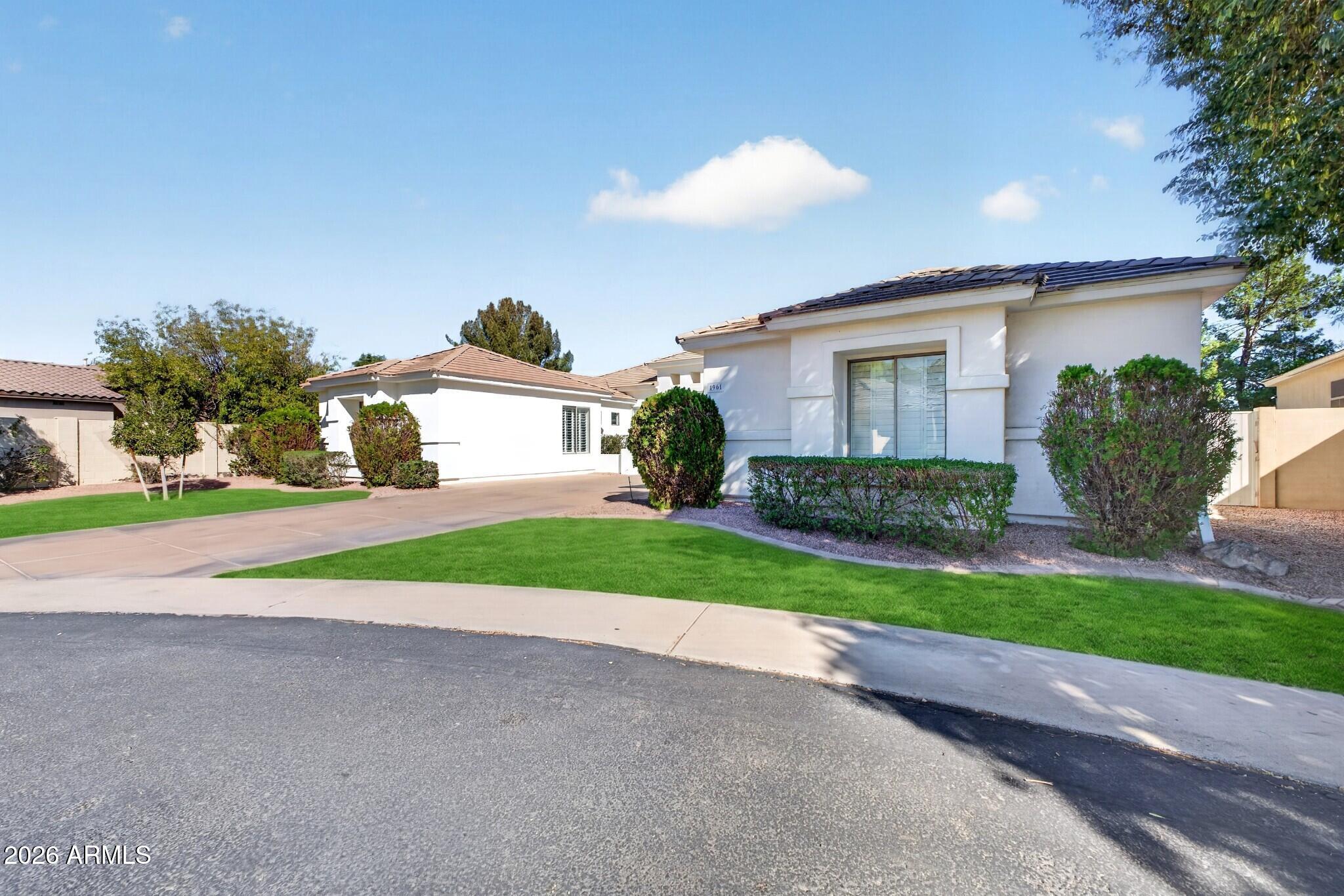 White single-story home with a tiled roof, trimmed shrubs, lawn, and driveway.