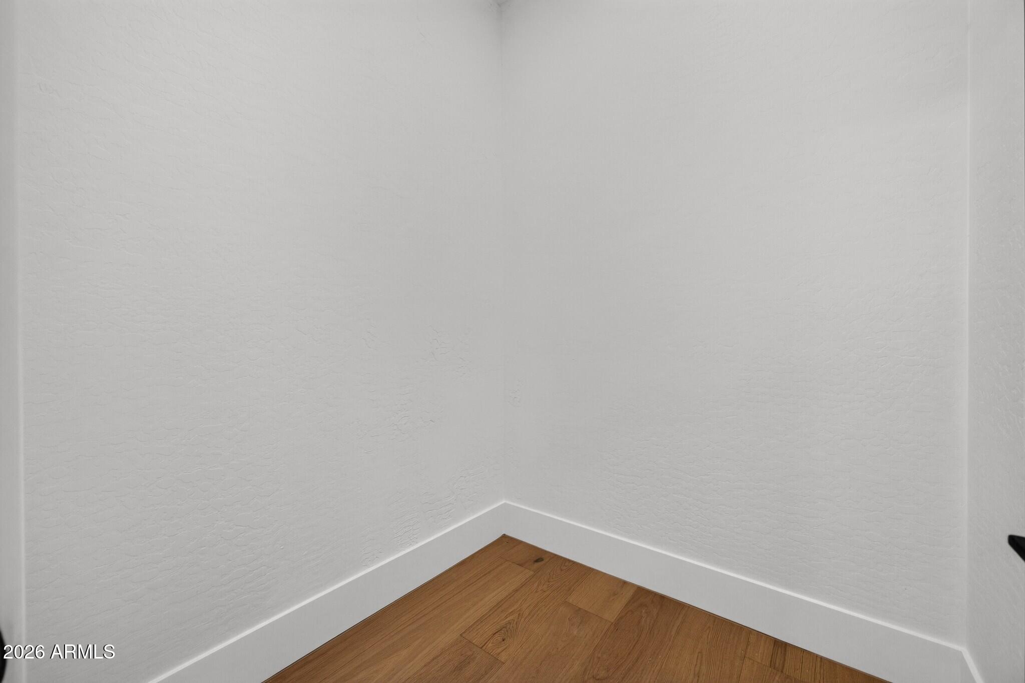Empty interior corner with textured white walls, white baseboards, and warm wood plank flooring.