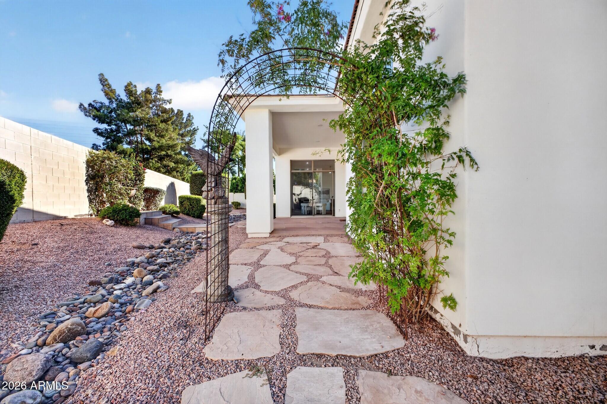 Side courtyard with a flagstone path, metal garden arch, climbing greenery, and covered patio.