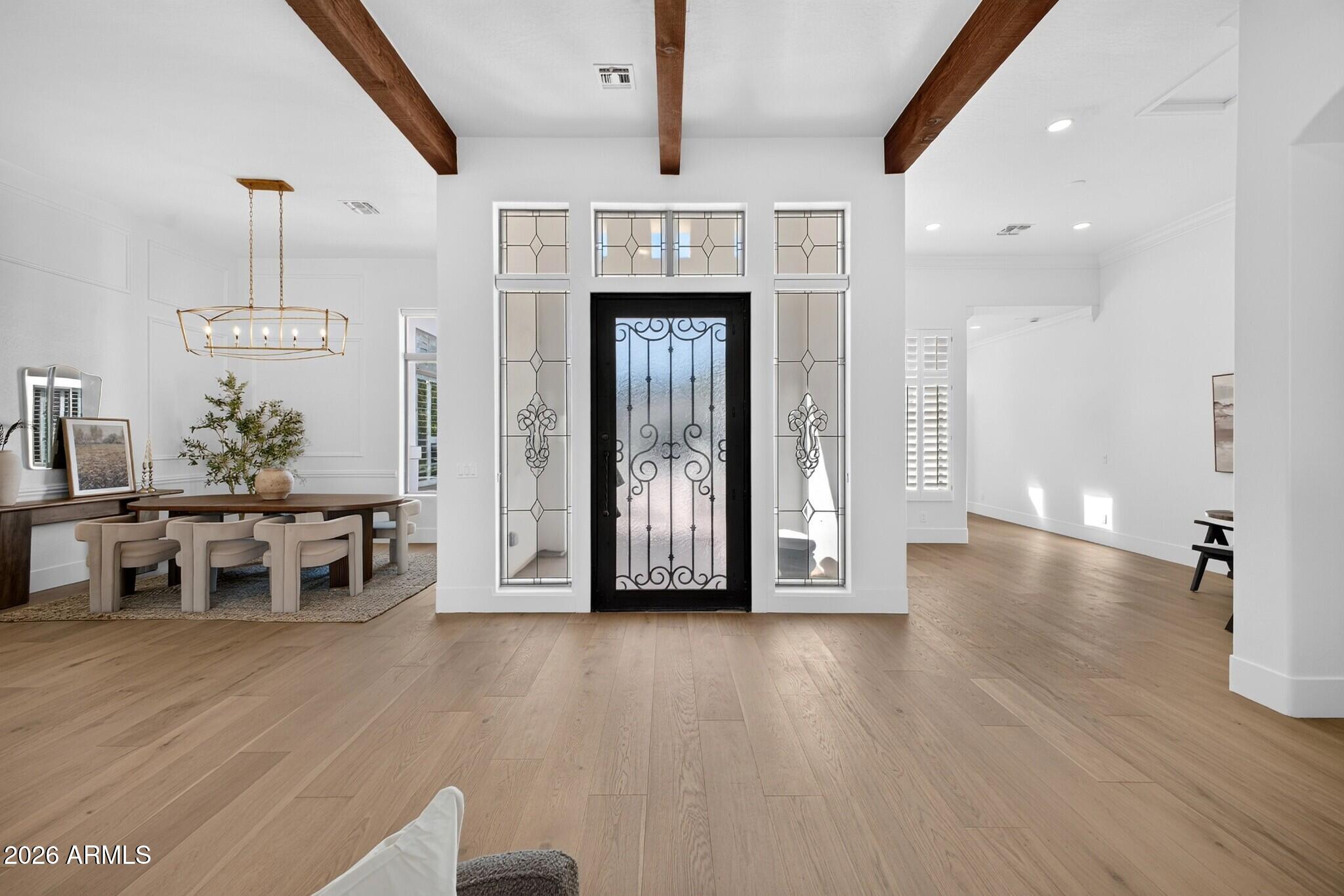 Foyer with a decorative iron-and-glass front door, exposed wood beams, light flooring, and dining area.