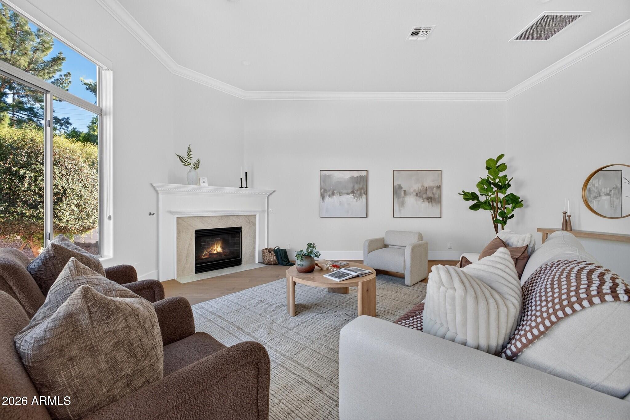 Furnished living room with a fireplace, large window, and neutral sofas.