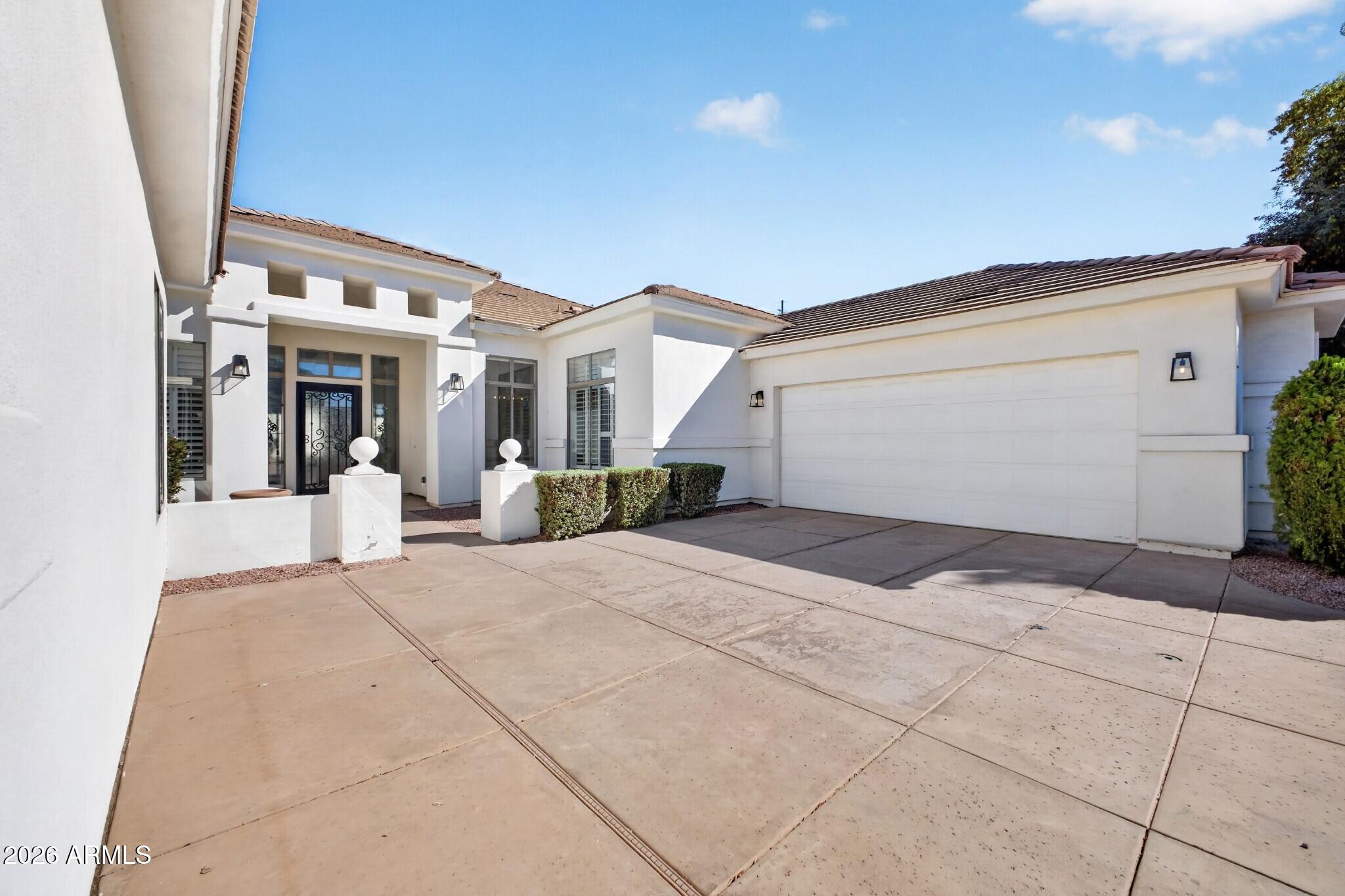 White stucco home with a decorative black front door, trimmed shrubs, and a wide driveway to the two-car garage.
