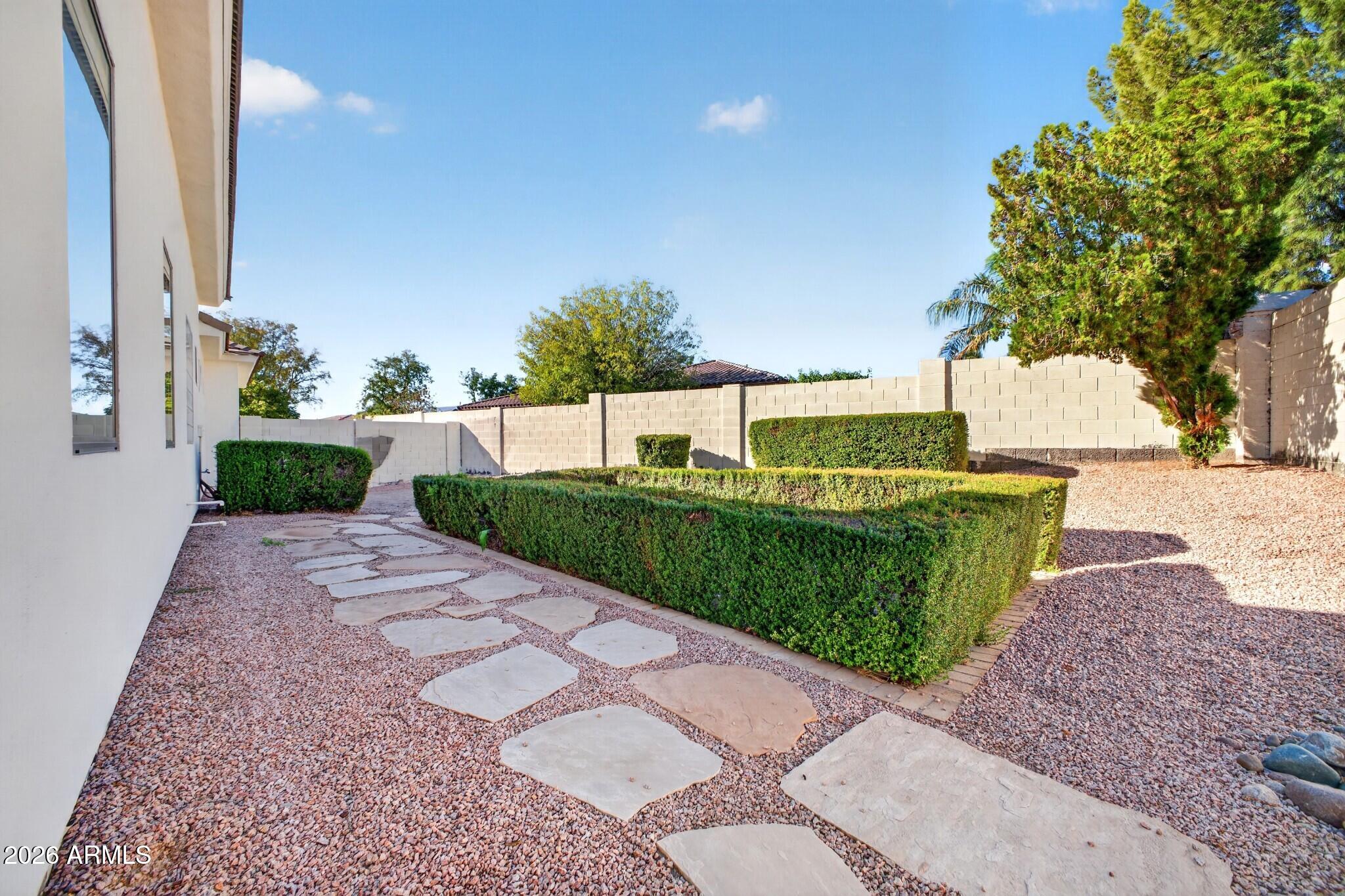 Landscaped side yard with gravel, stone stepping path, clipped hedges, and a block wall.