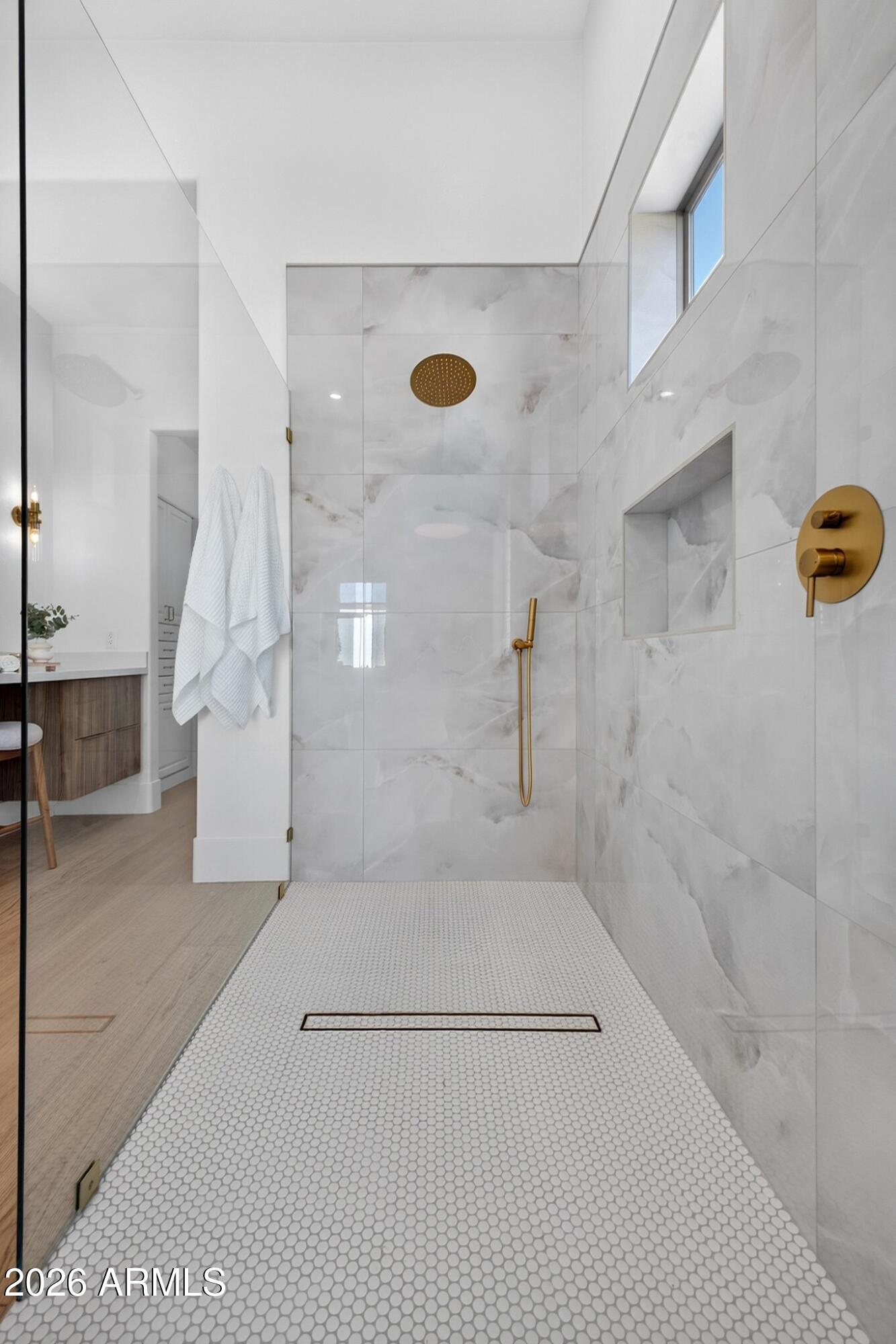 Walk-in shower with marble-look walls, white hex tile floor, and brass fixtures.
