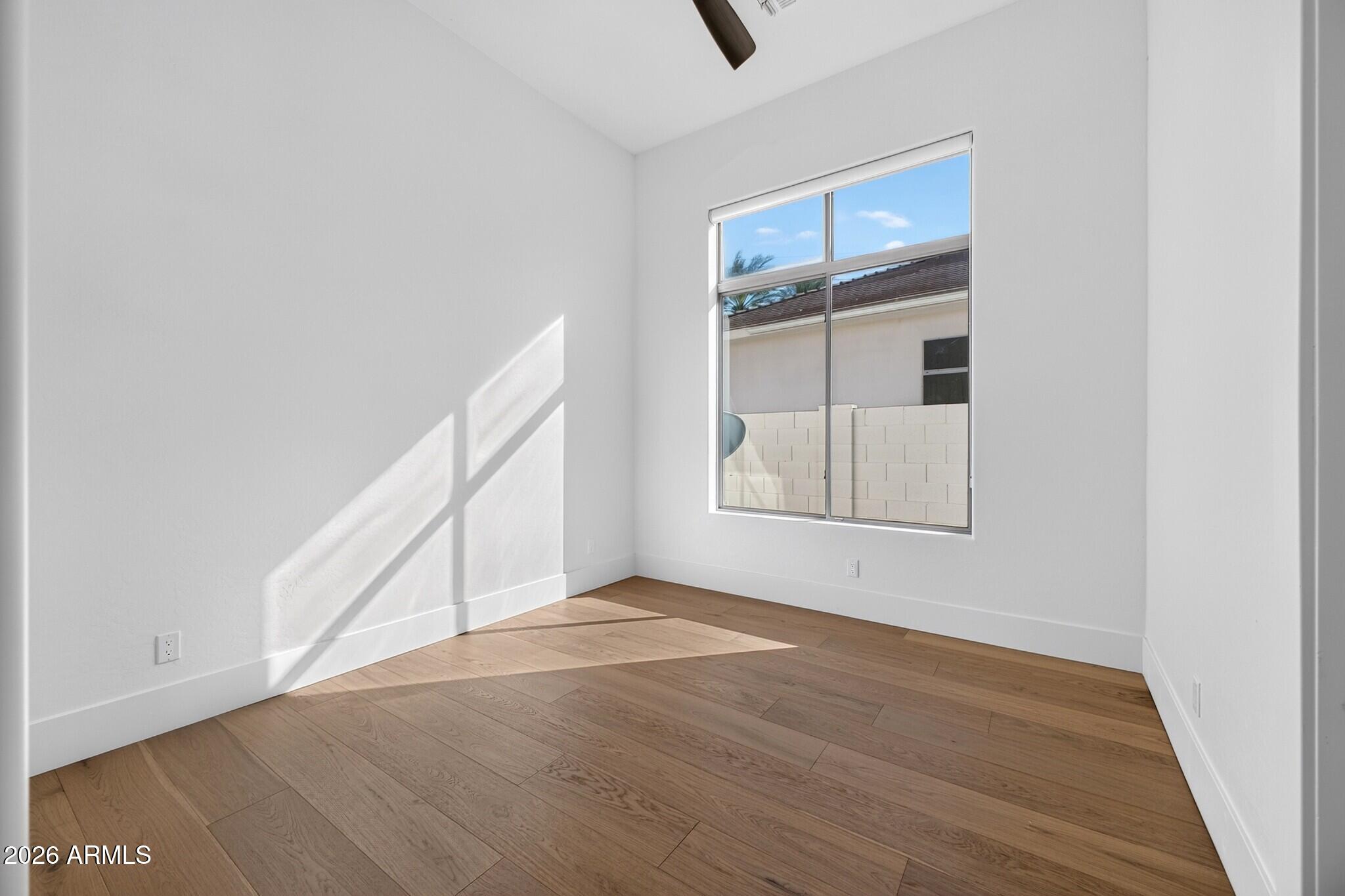 Empty room with light wood flooring, a ceiling fan, and a large sunlit window.