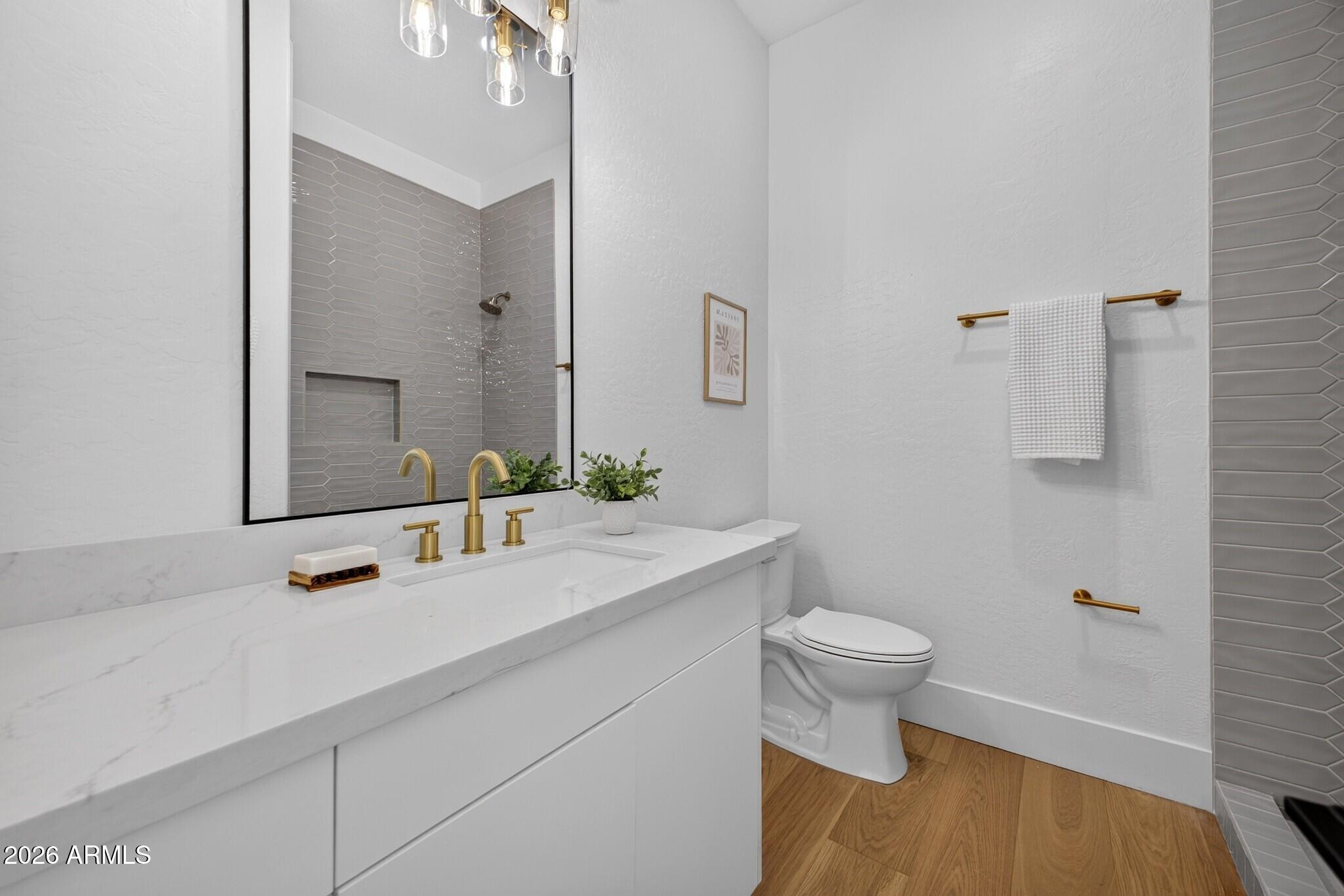 Bathroom with a white vanity, brass fixtures, gray tiled shower, and wood-look floor.