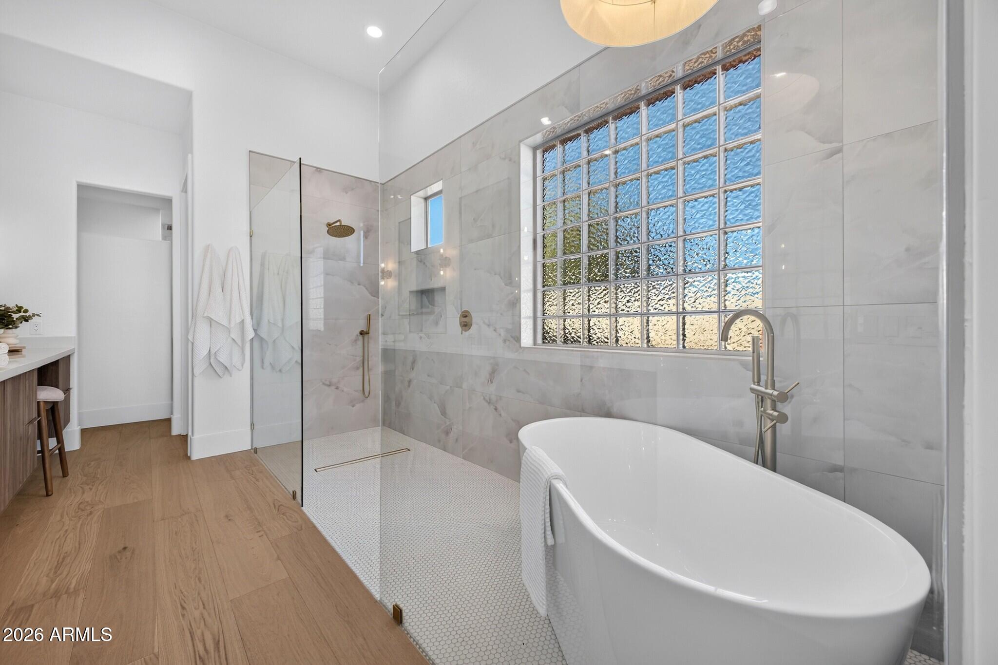 Modern bathroom with a freestanding tub, glass-enclosed shower, gray tile, and large glass-block window.