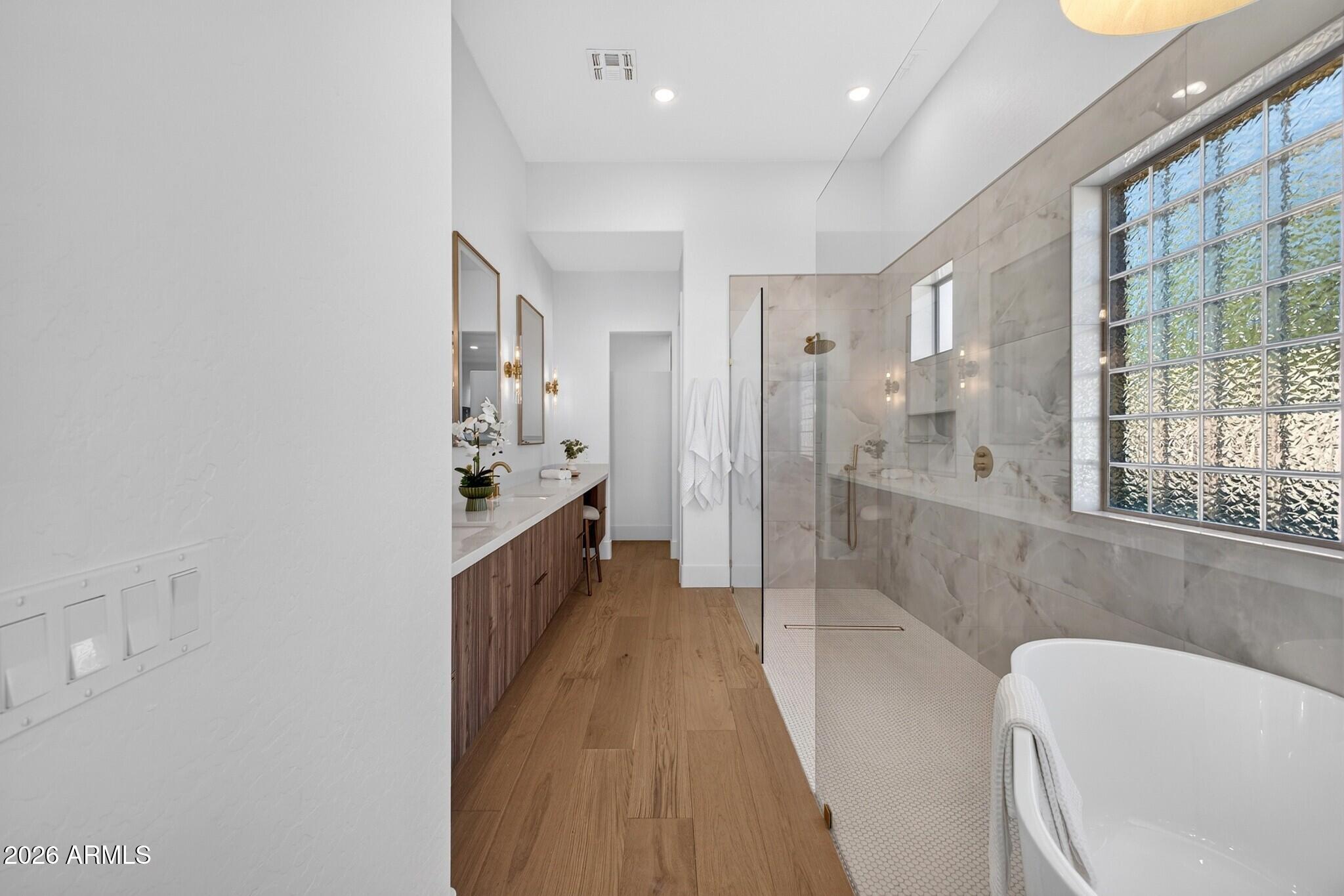Modern bathroom with a glass shower, freestanding tub, marble-look tile, and large grid window.