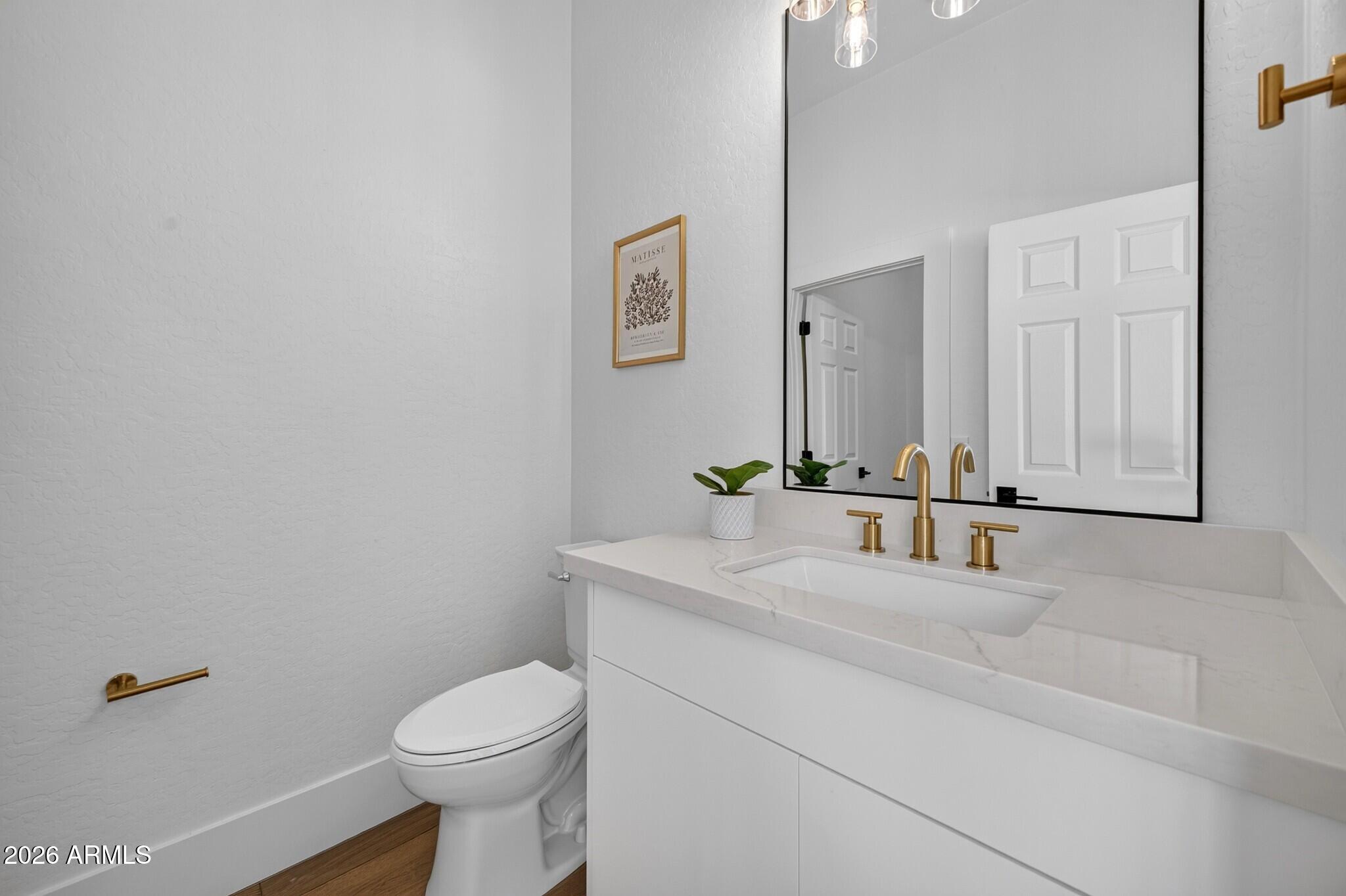 Modern bathroom with a white vanity, brass fixtures, large mirror, and toilet.