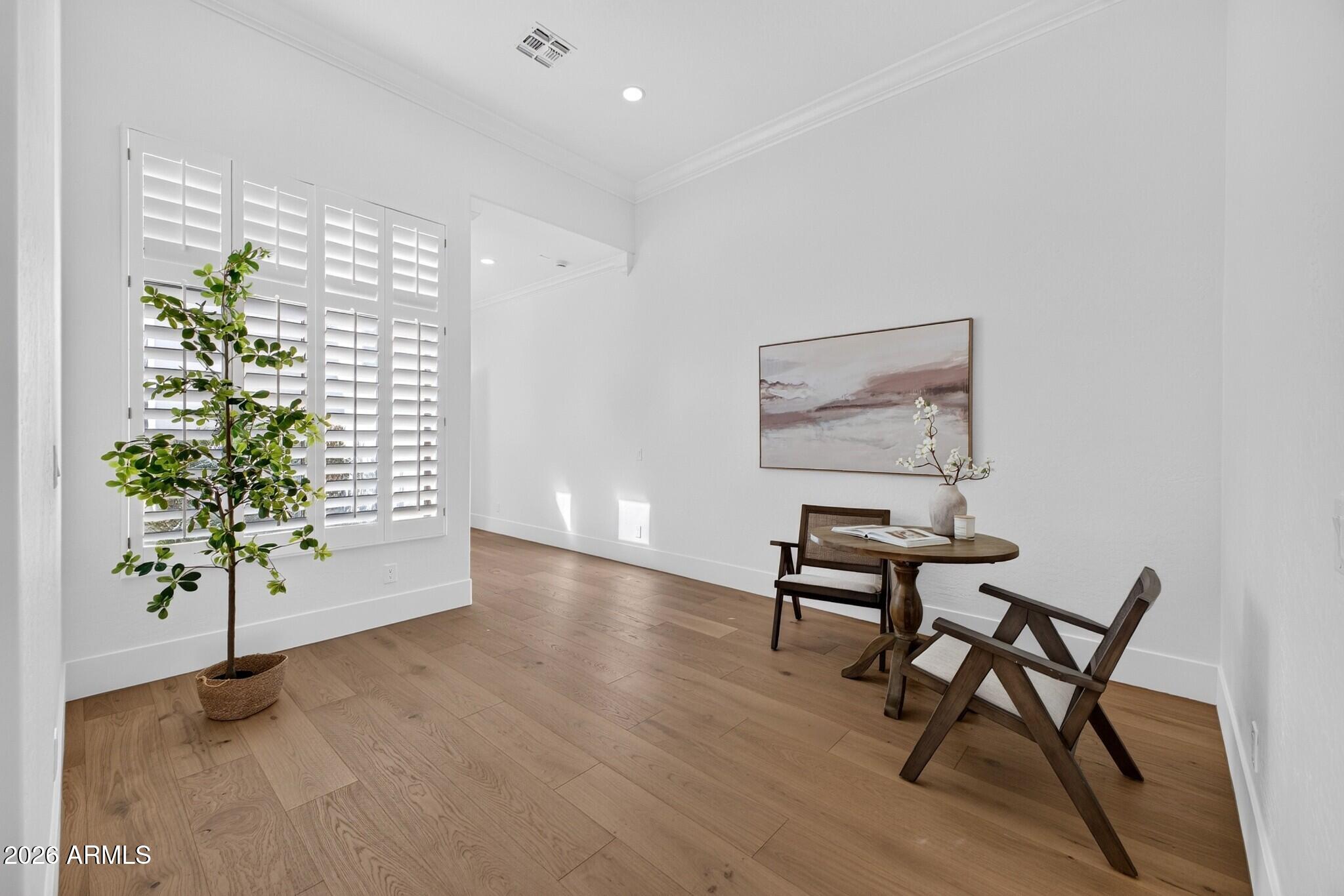 Bright staged room with plantation shutters, wood floors, and a small table with two chairs.