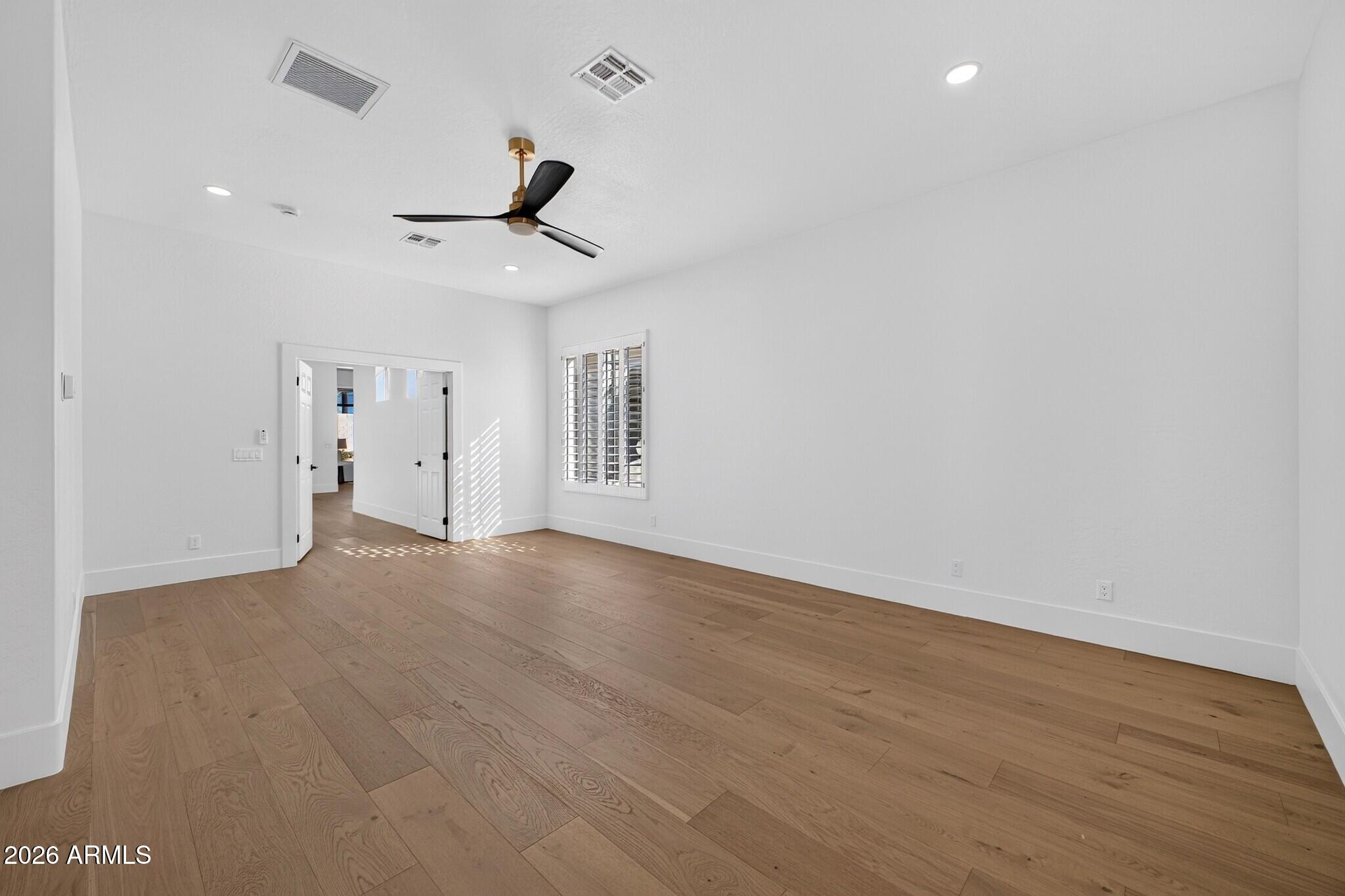 Vacant room with light wood floors, a black ceiling fan, and a shuttered window beside open double doors.