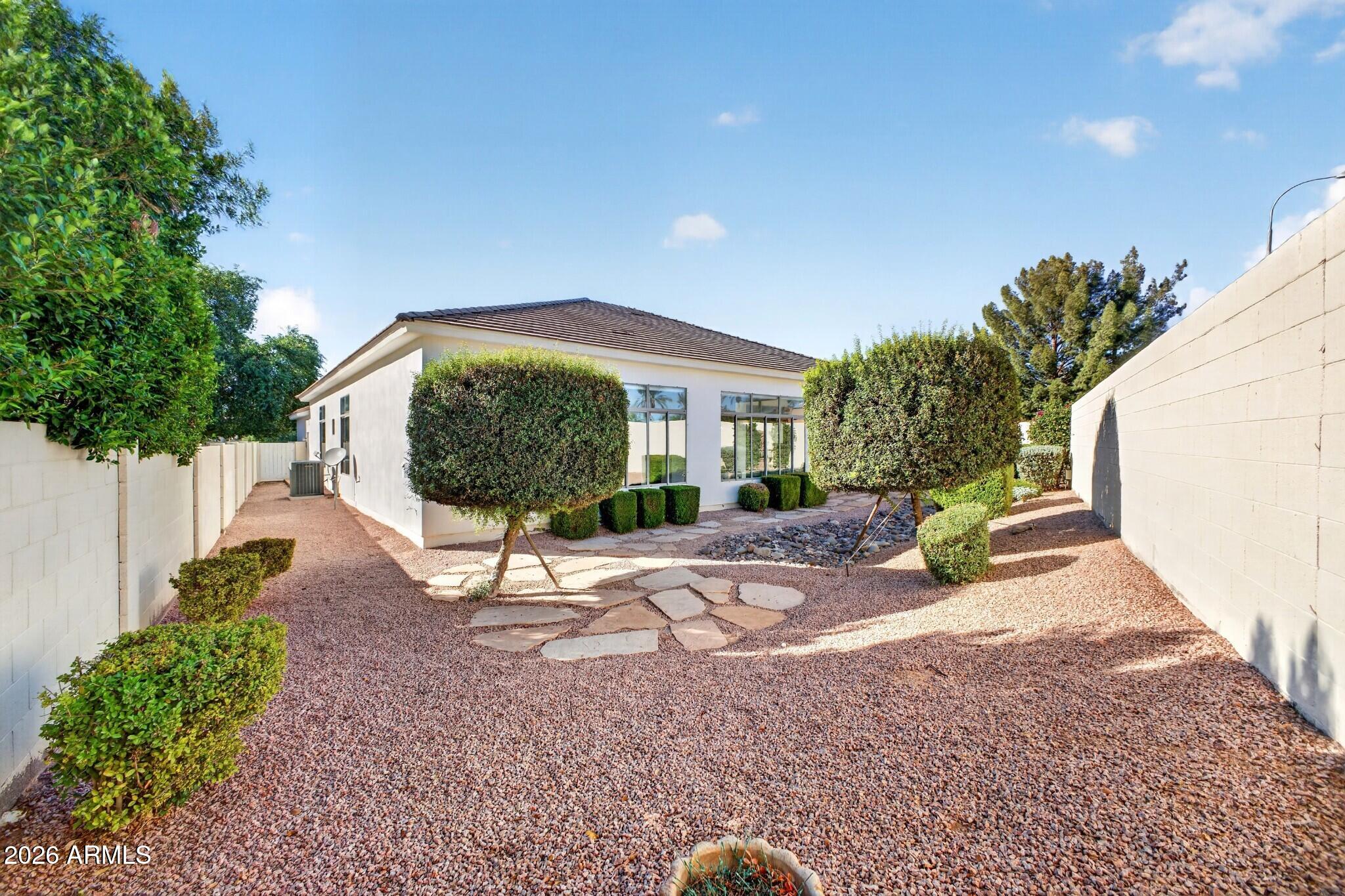 Single-story home behind a gravel yard with trimmed trees, stepping stones, and a dry rock bed.