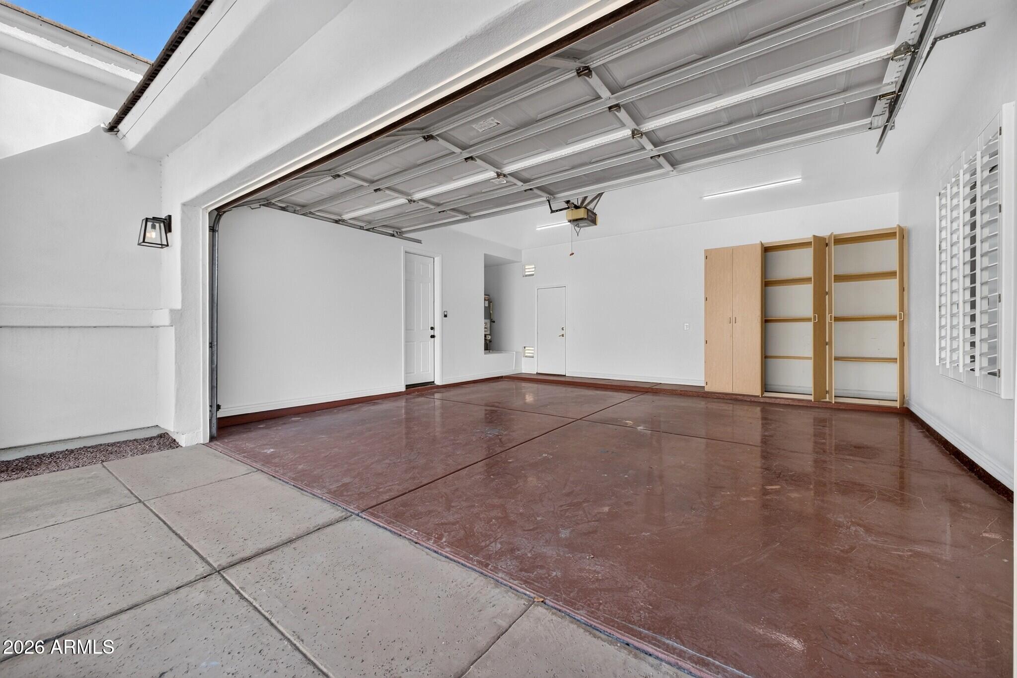 Empty garage with open overhead door, glossy reddish-brown floor, and built-in wooden cabinets.