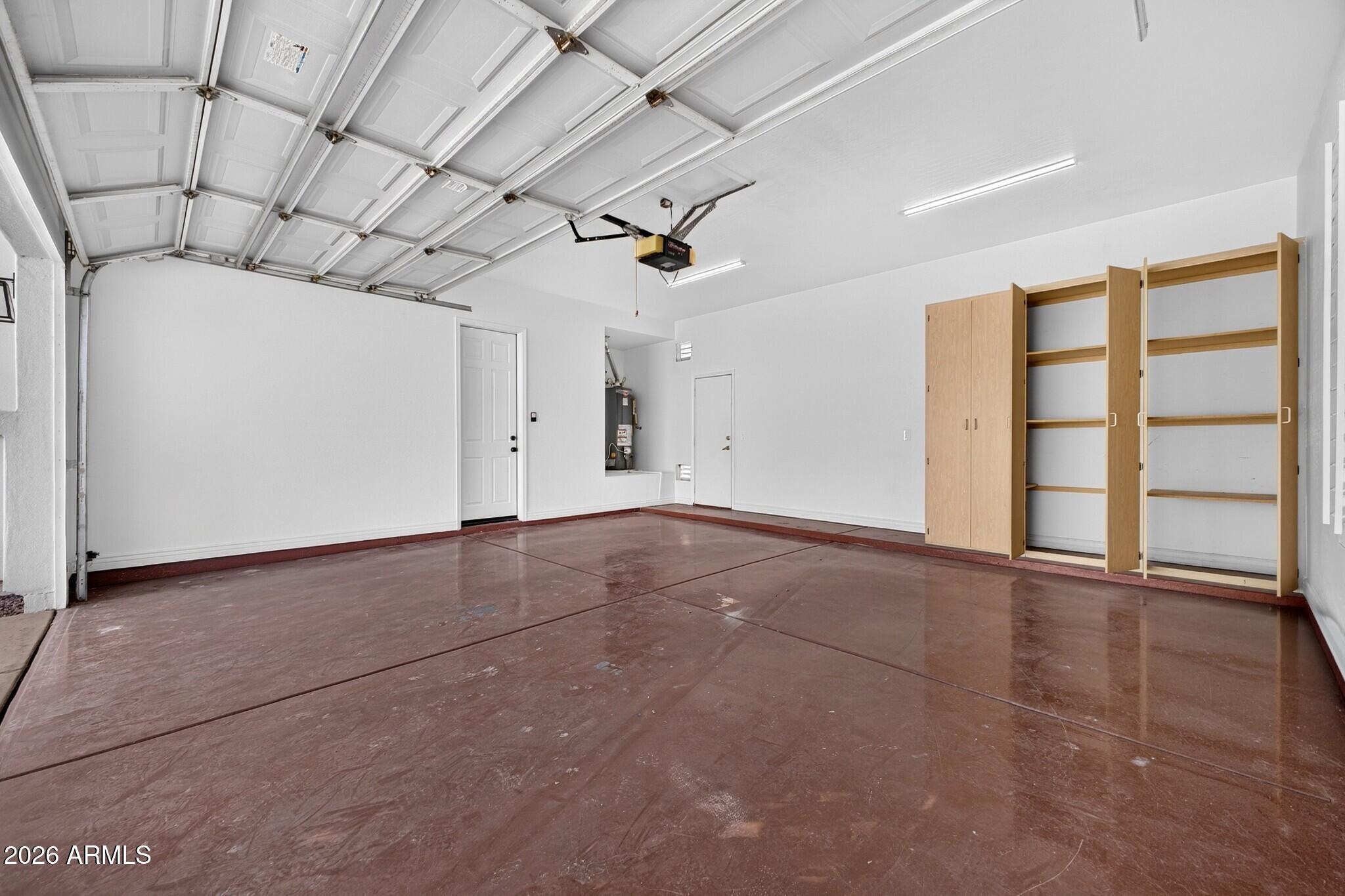 Vacant garage with a raised overhead door, brown concrete floor, and built-in wooden storage cabinets.