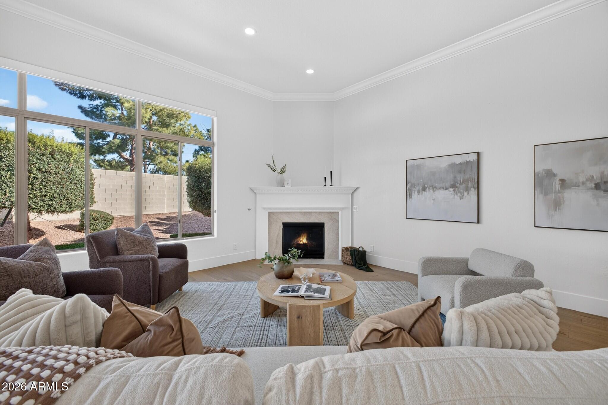 Staged living room with a white fireplace, large windows overlooking the yard, and neutral seating.