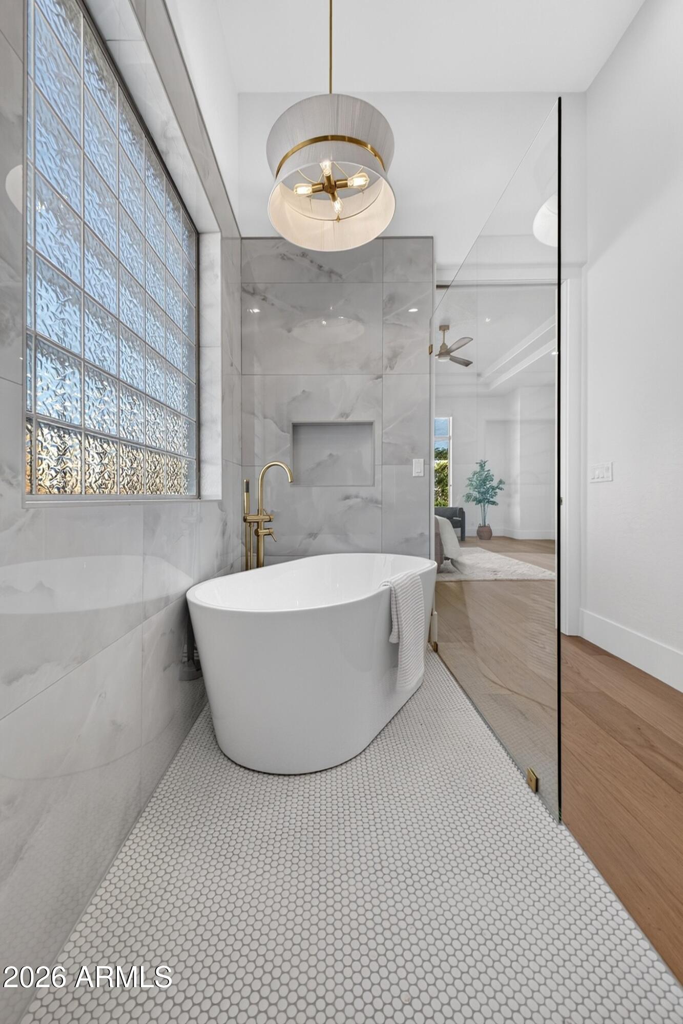 Modern bathroom with a freestanding tub, brass faucet, and textured glass-block window