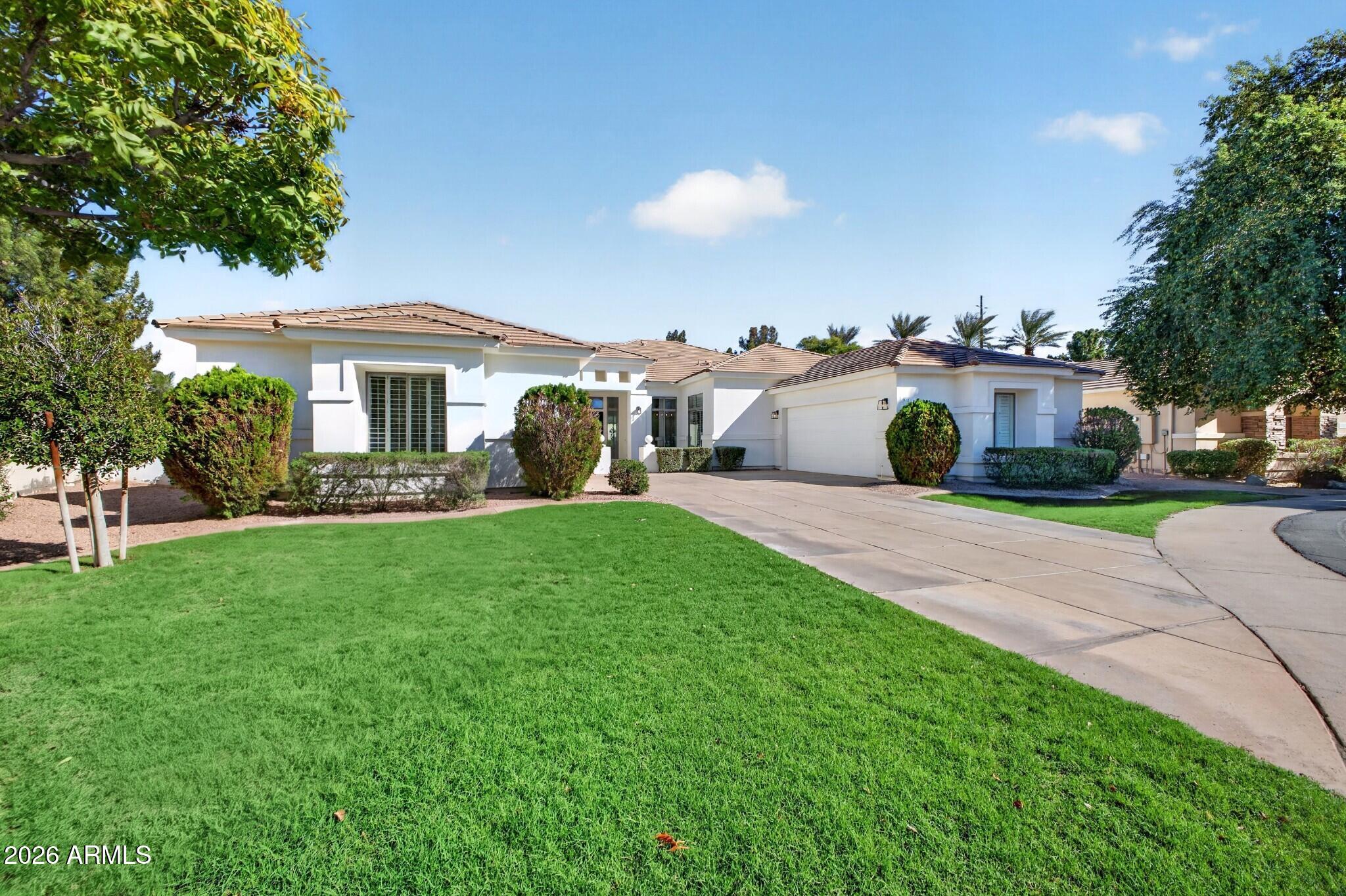 Single-story white stucco home with a tile roof, attached garage, broad driveway, and manicured lawn.