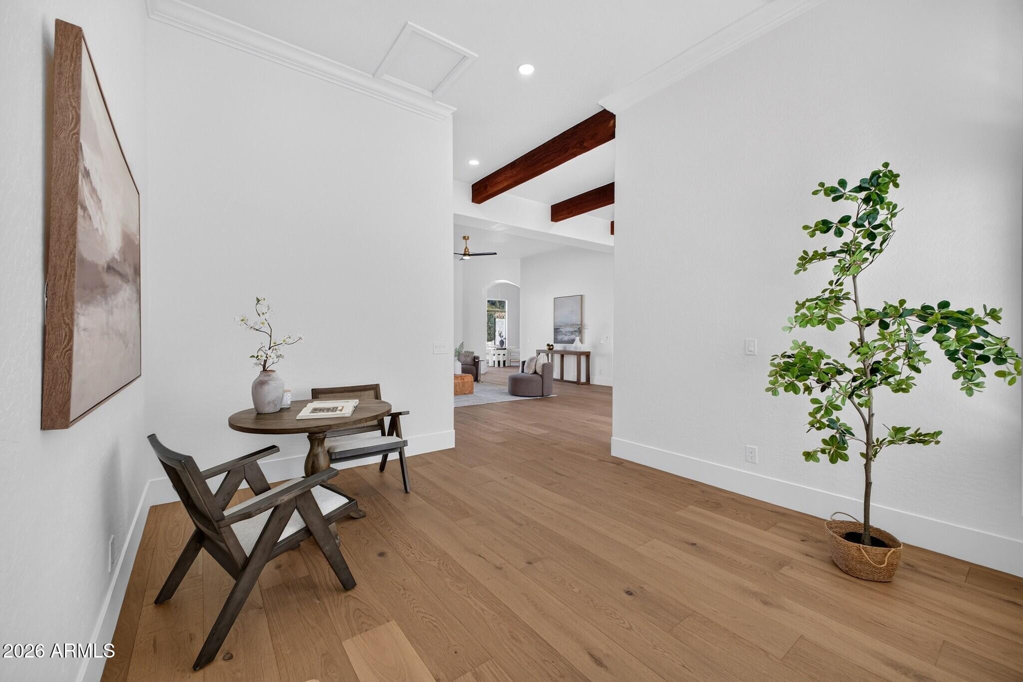 Bright entry with wood floors, a round table and chairs, potted tree, and exposed ceiling beams.