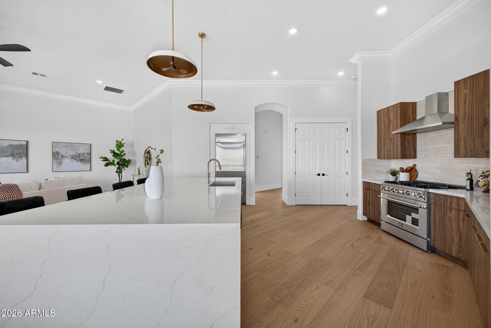 Open-plan kitchen with a white stone island, wood cabinetry, and stainless steel range.