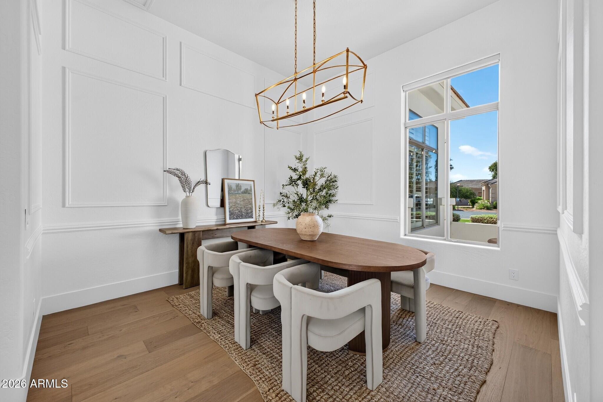 Dining room with an oval wood table, white upholstered chairs, paneled walls, and a brass chandelier.
