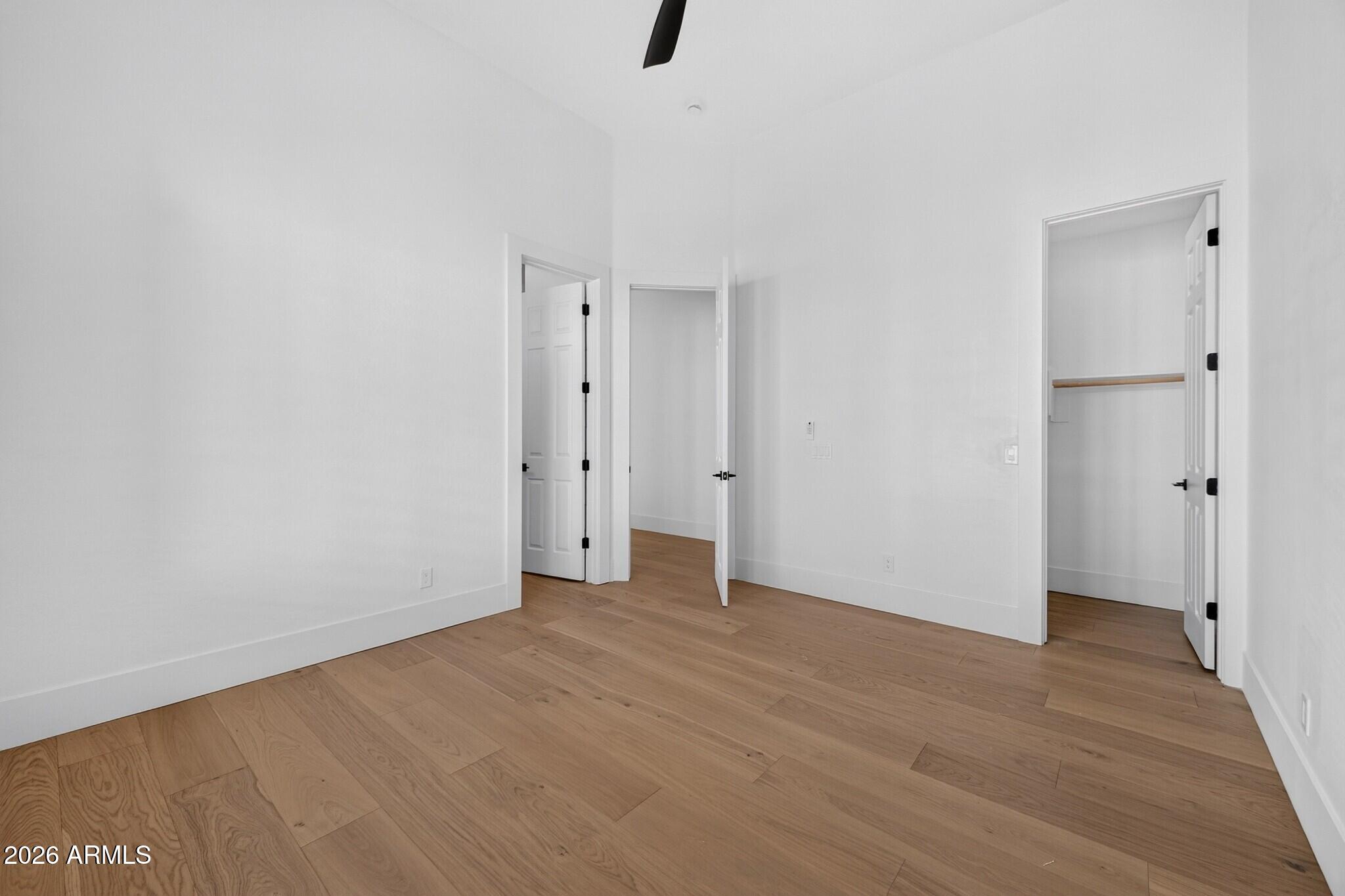 Empty room with light wood flooring, white walls, and three open doorways.