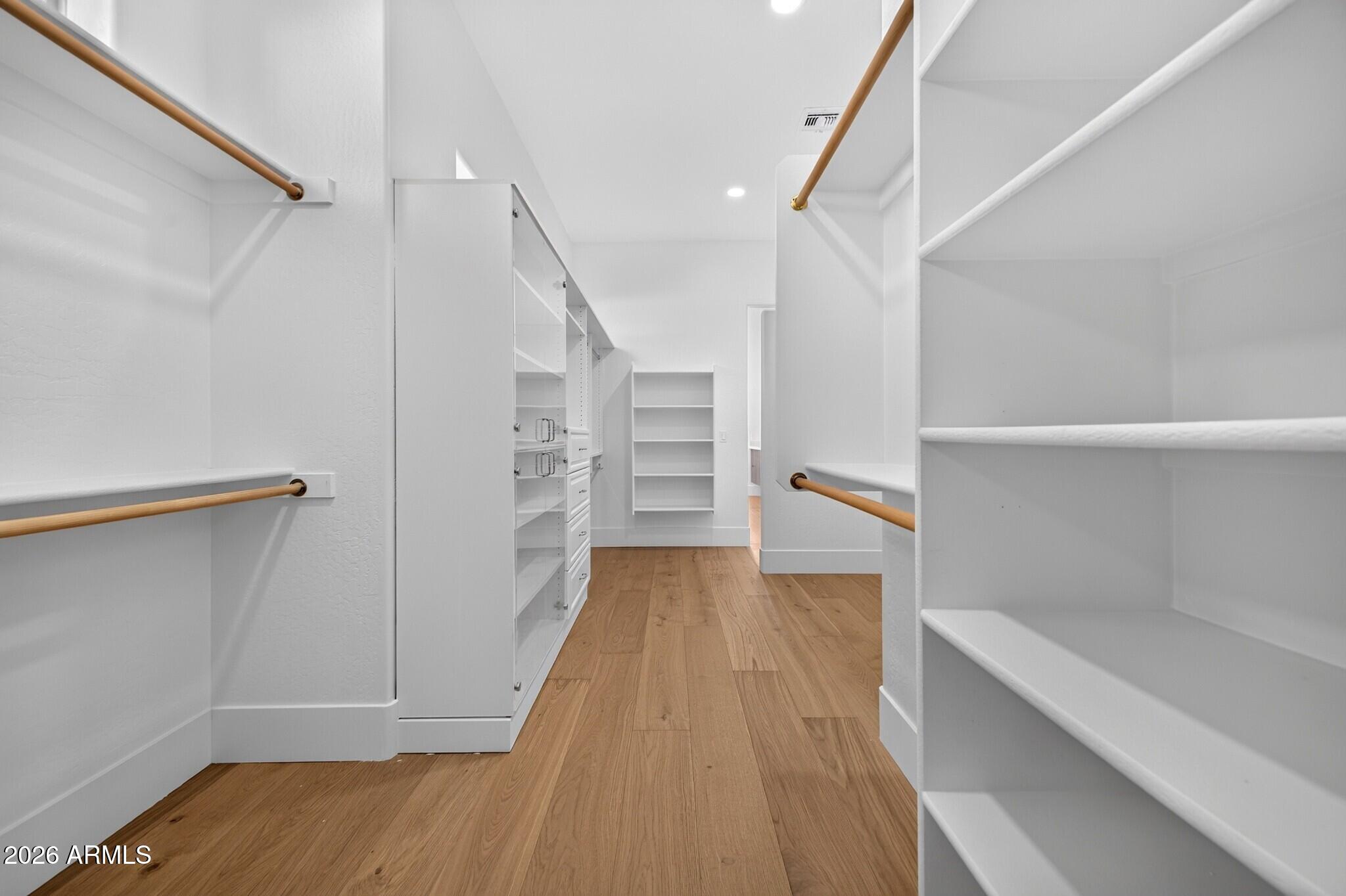 Walk-in closet with white built-in shelving, drawers, brass hanging rods, and wood flooring.