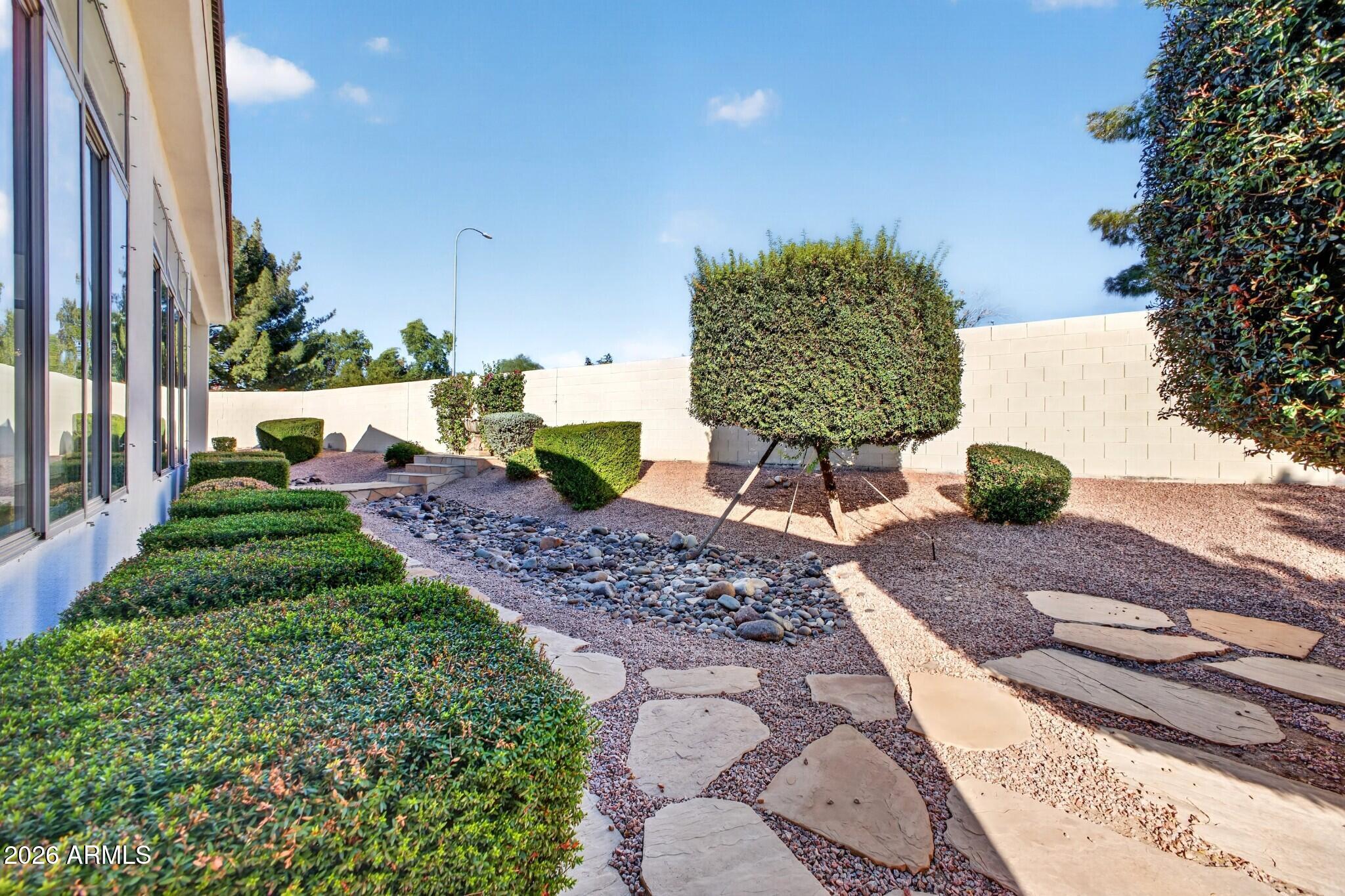 Side yard with gravel landscaping, a dry rock stream, stepping stones, and neatly trimmed shrubs.