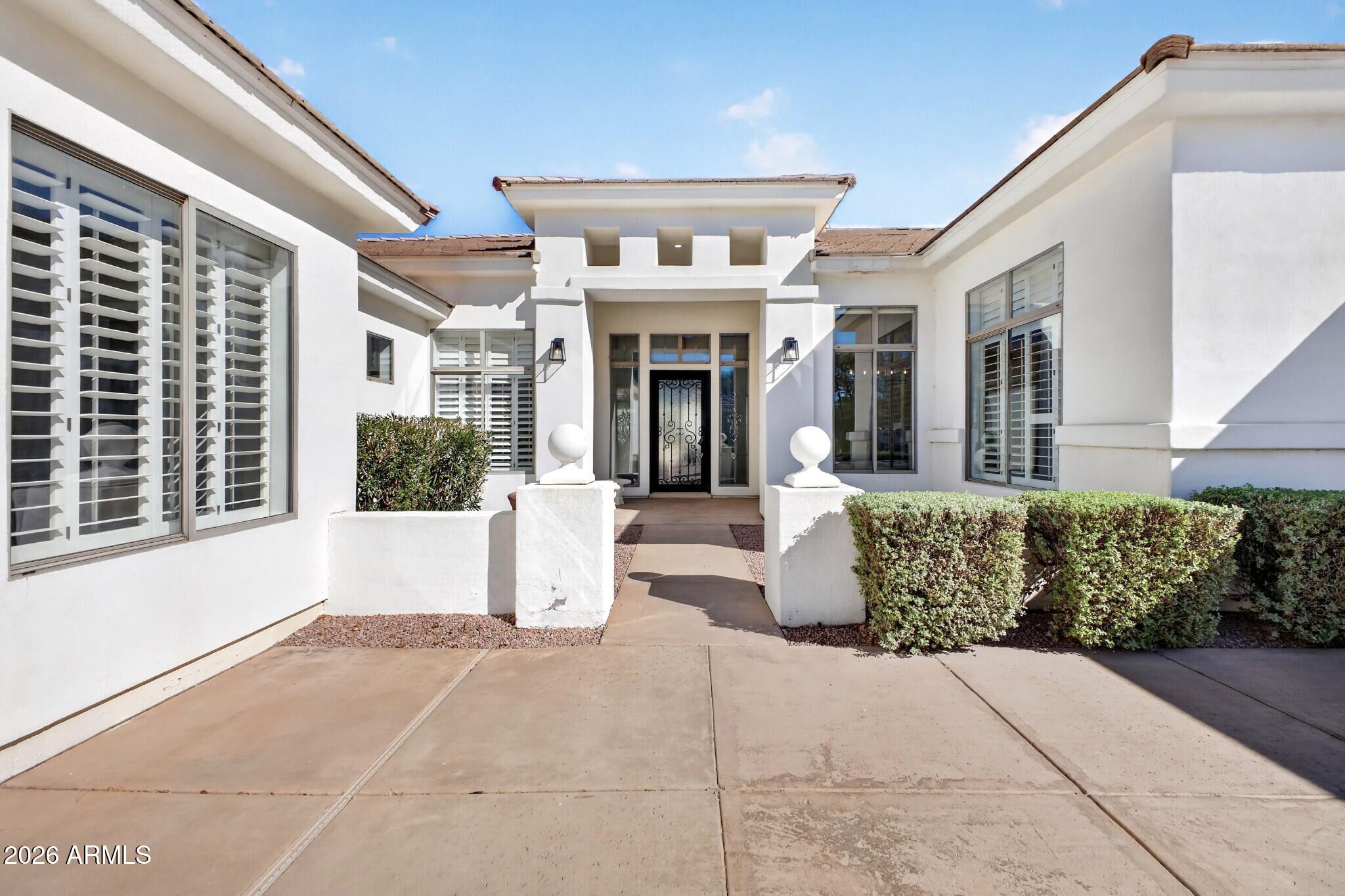 White stucco home with a recessed entry, black metal front door, shuttered windows, and trimmed hedges.