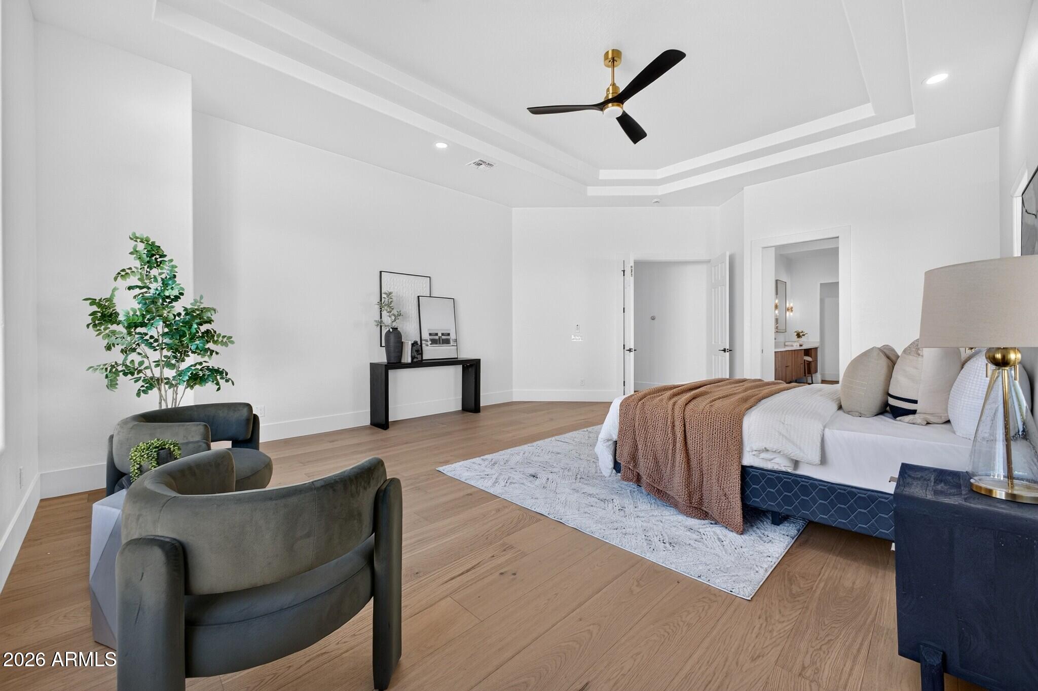 Staged bedroom with a king bed, brown knit throw, upholstered chairs, and a tray ceiling with a black fan.