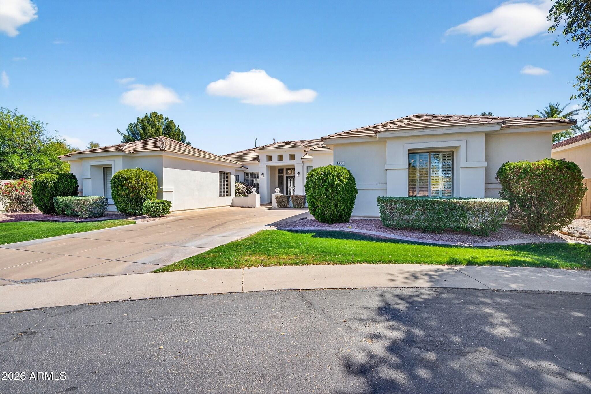 Single-story white stucco home with a tiled roof, landscaped front yard, and broad driveway.