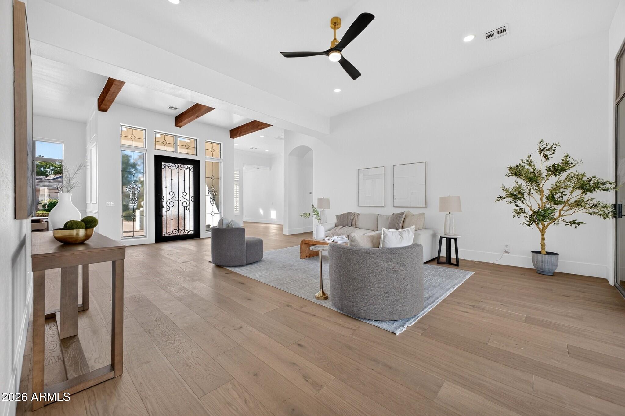 Staged living room with a black glass-paneled entry door, exposed wood beams, and light wood flooring.