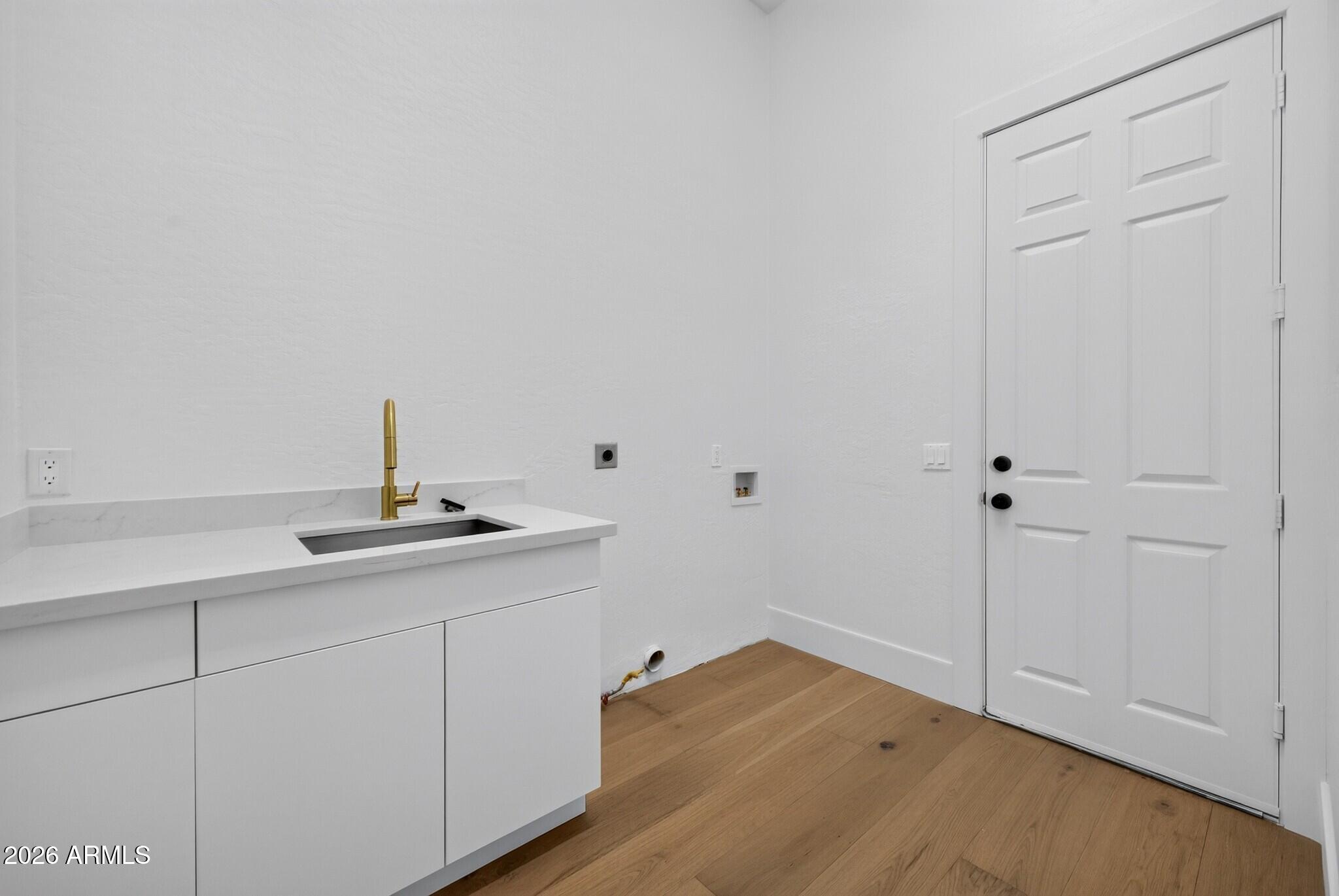 Laundry room with white cabinets, a brass-faucet sink, laundry hookups, and wood flooring.
