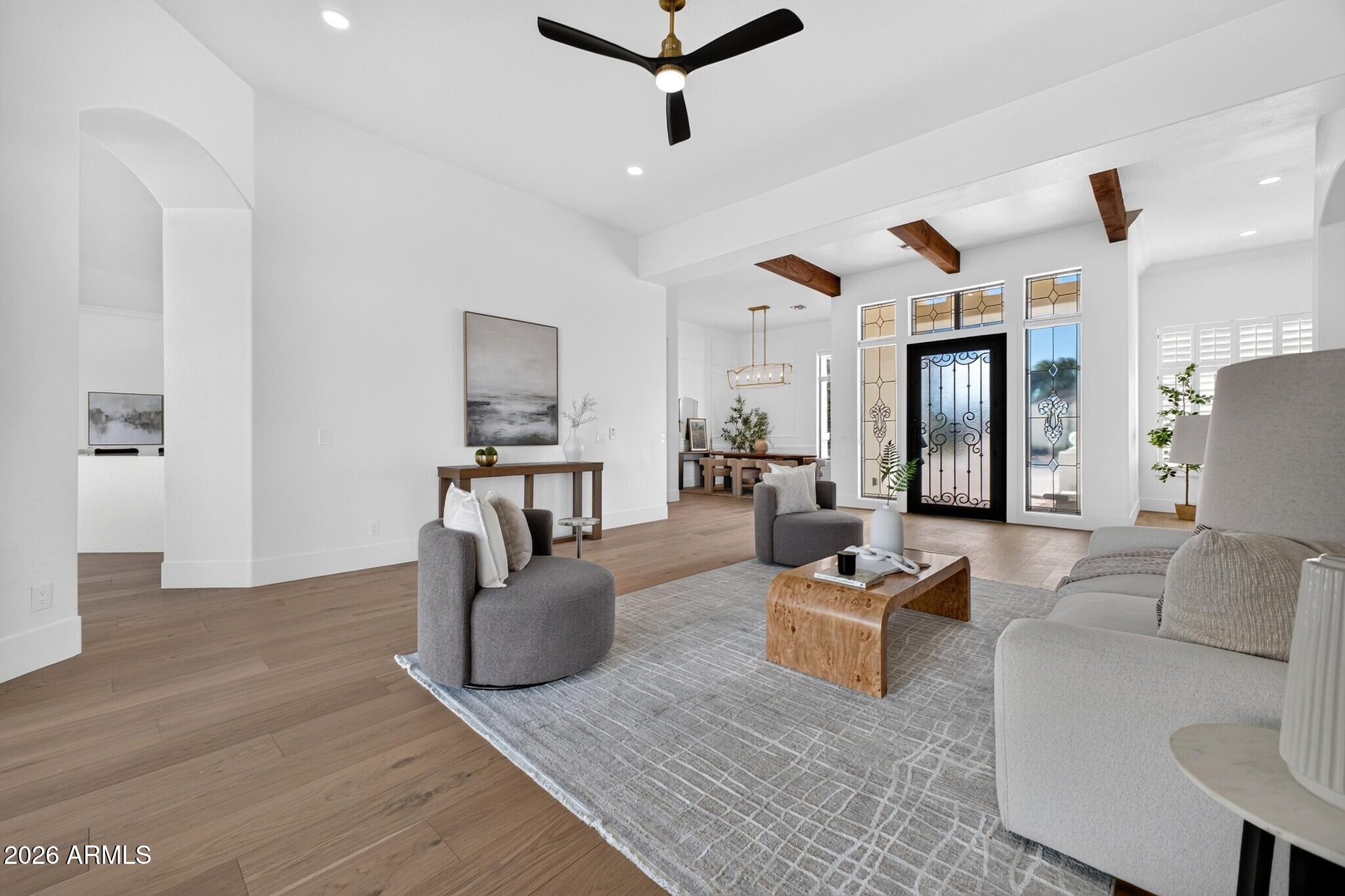 Furnished living room with exposed wood beams, gray seating, and a decorative glass front door.
