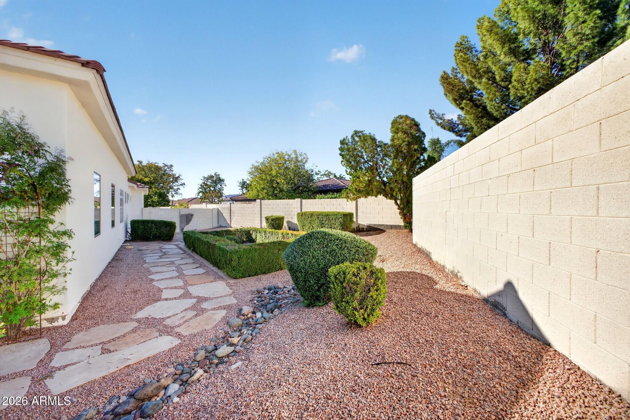 Side yard with a flagstone path, gravel landscaping, trimmed shrubs, and a tall block wall.