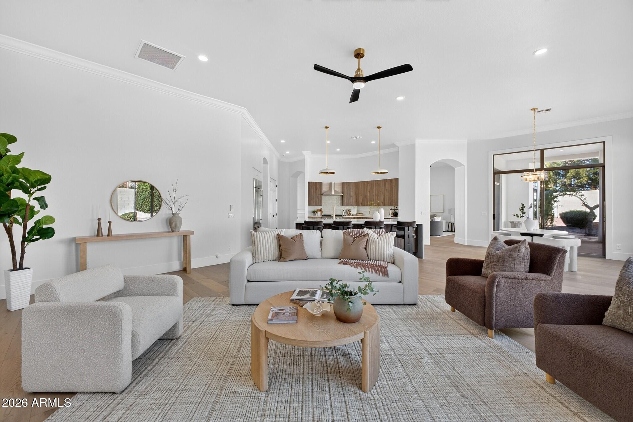 Open-plan living room with a white sofa, textured armchairs, and a wood-cabinet kitchen.