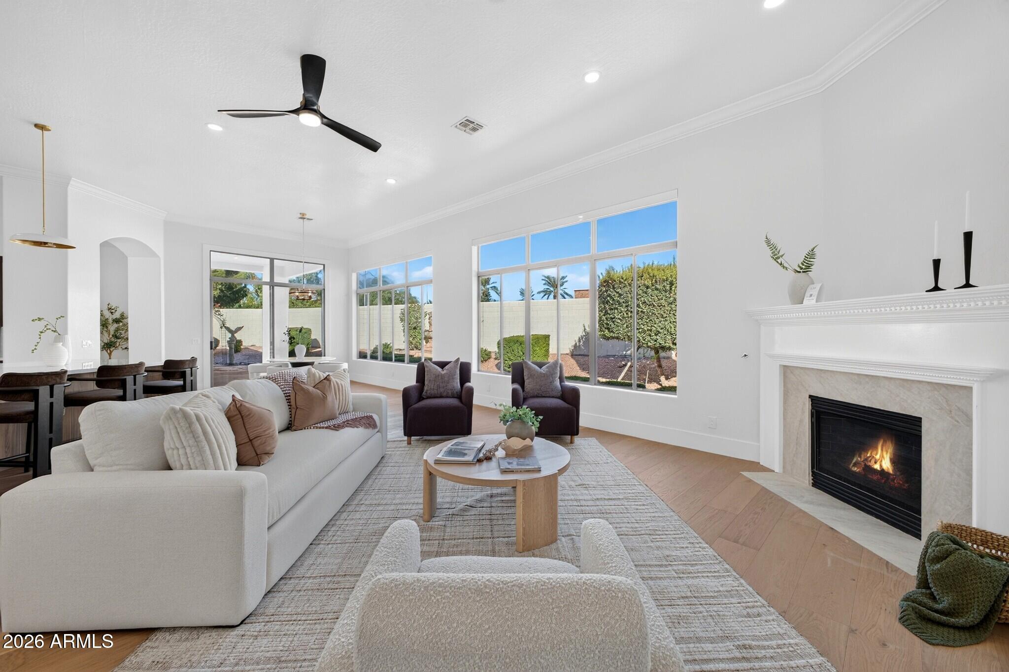 Furnished living room with large backyard-facing windows and a lit fireplace.
