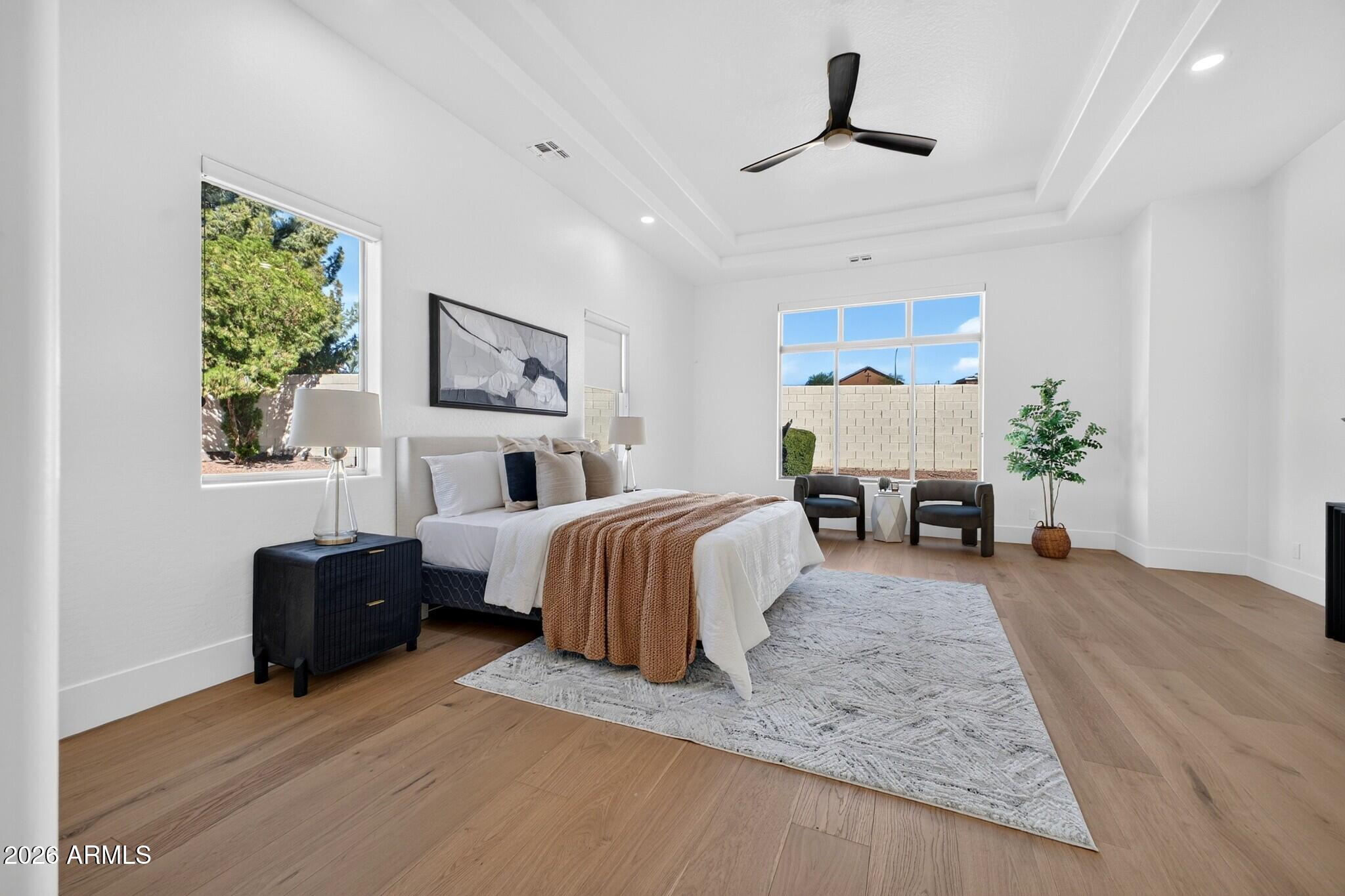 Staged bedroom with a large white bed, rust-colored throw, tray ceiling, and light wood floors.