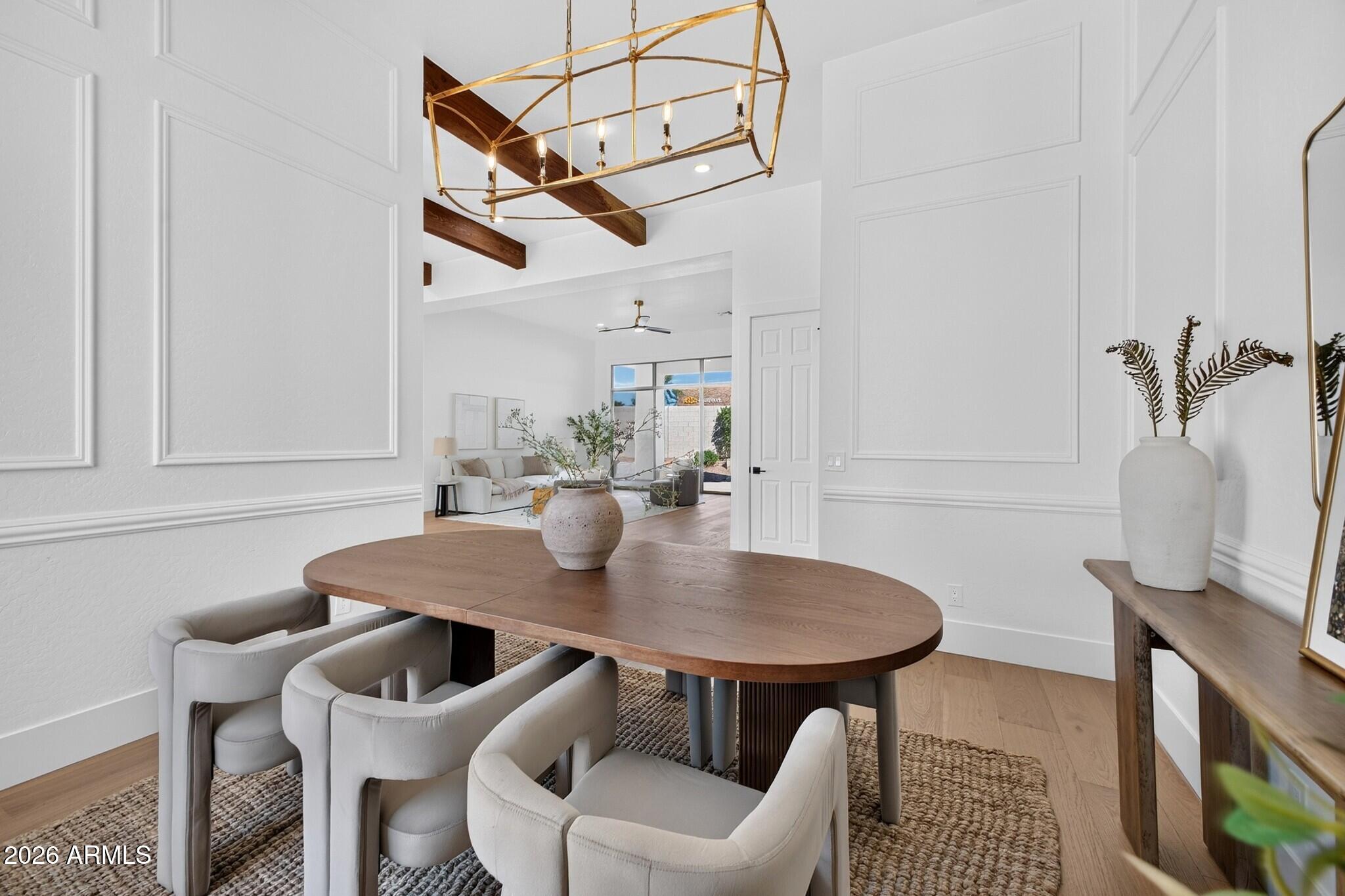 Dining room with an oval wood table, upholstered chairs, and a brass chandelier opening to the living area.