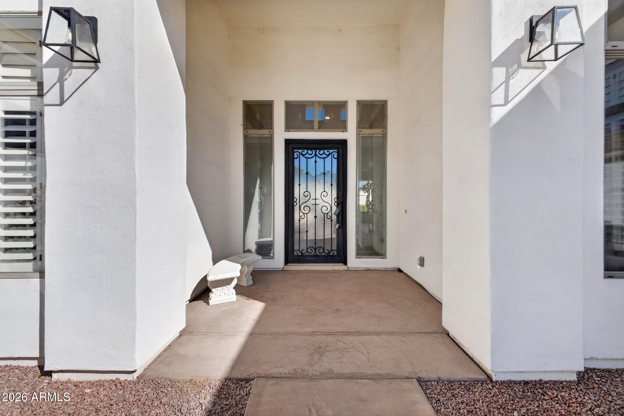 Covered home entry with a decorative iron security door, glass sidelights, and a white bench.