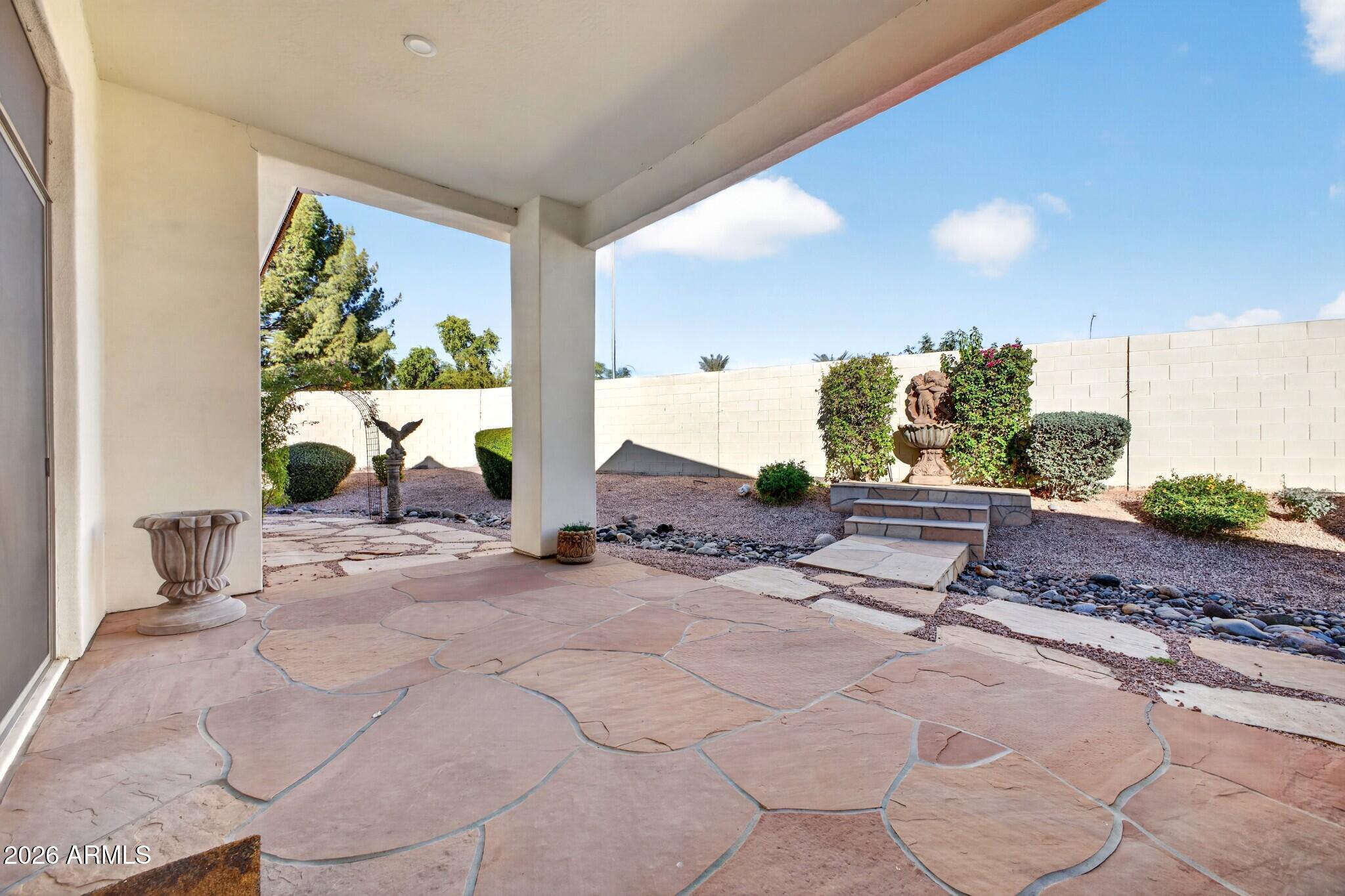 Covered flagstone patio overlooking a gravel yard with a decorative fountain and flowering vines.