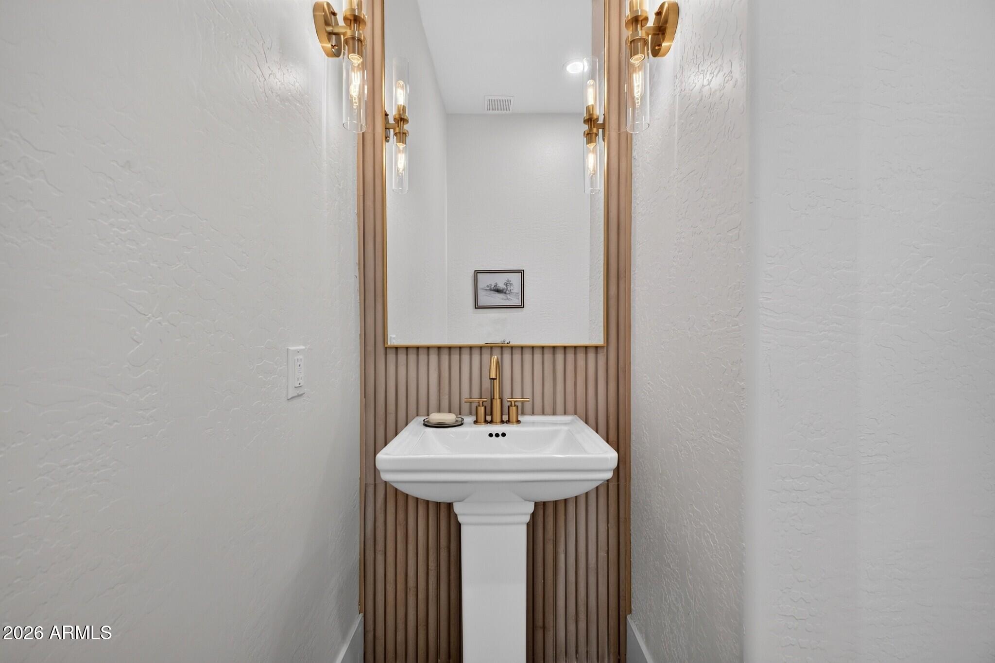 Powder room with a white pedestal sink, gold fixtures, and vertical wood-slat accent wall.