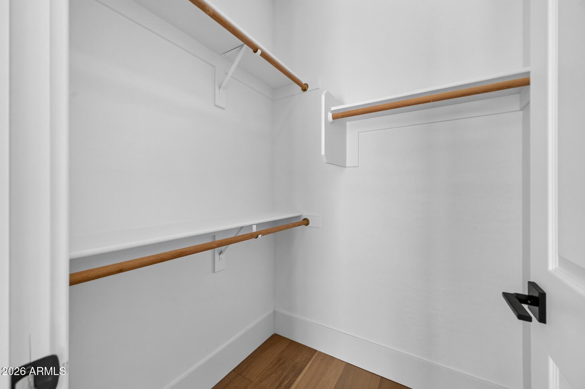 Empty walk-in closet with built-in shelves, wooden hanging rods, and wood-look flooring.