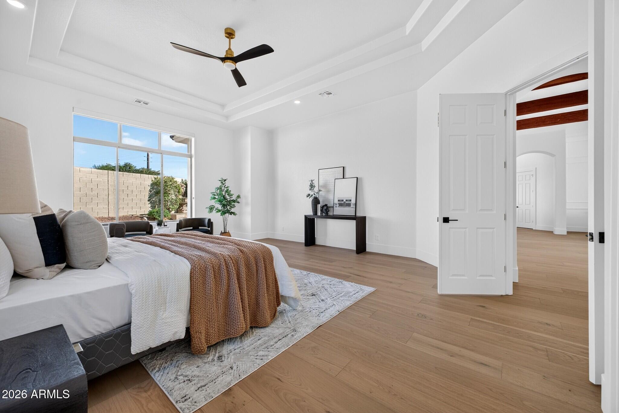 Staged bedroom with a brown throw on the bed, large window, wood-look floors, and tray ceiling.