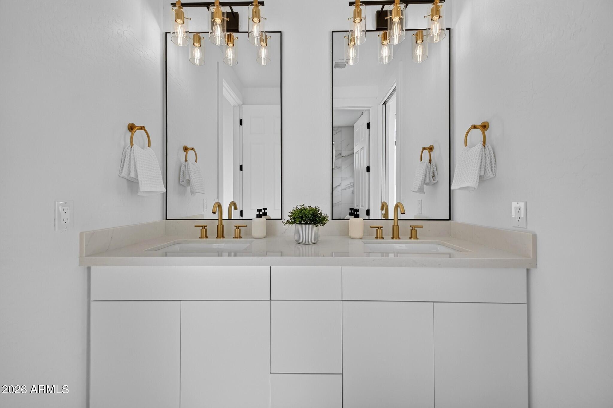 Double-sink bathroom vanity with white cabinetry, gold fixtures, and two large mirrors.