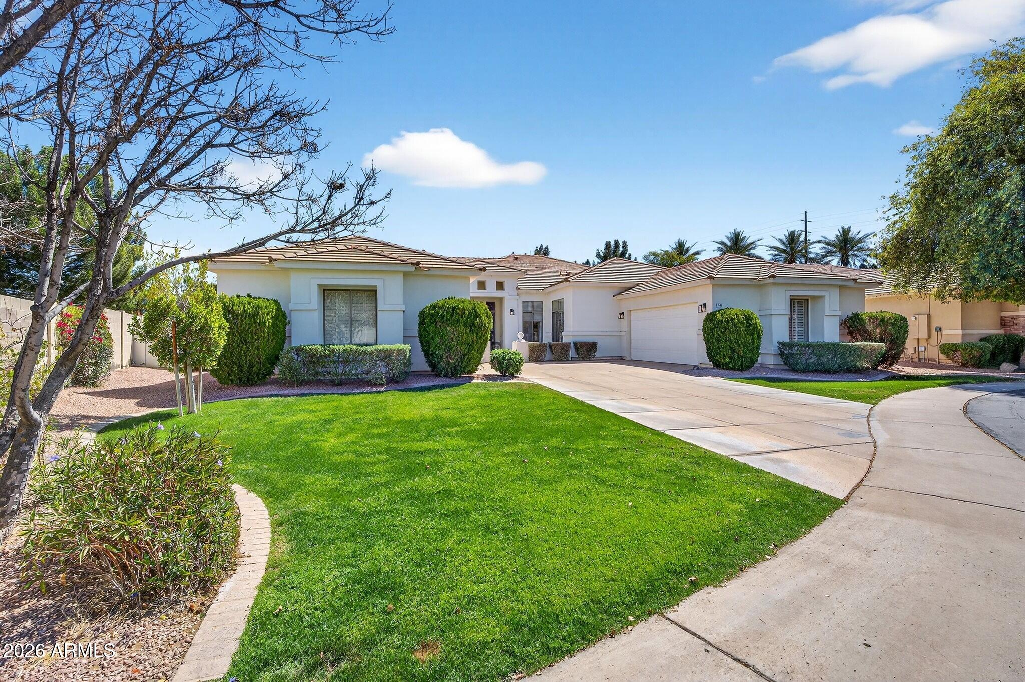 Single-story stucco home with tiled roof, attached garage, curved driveway, and green front lawn.