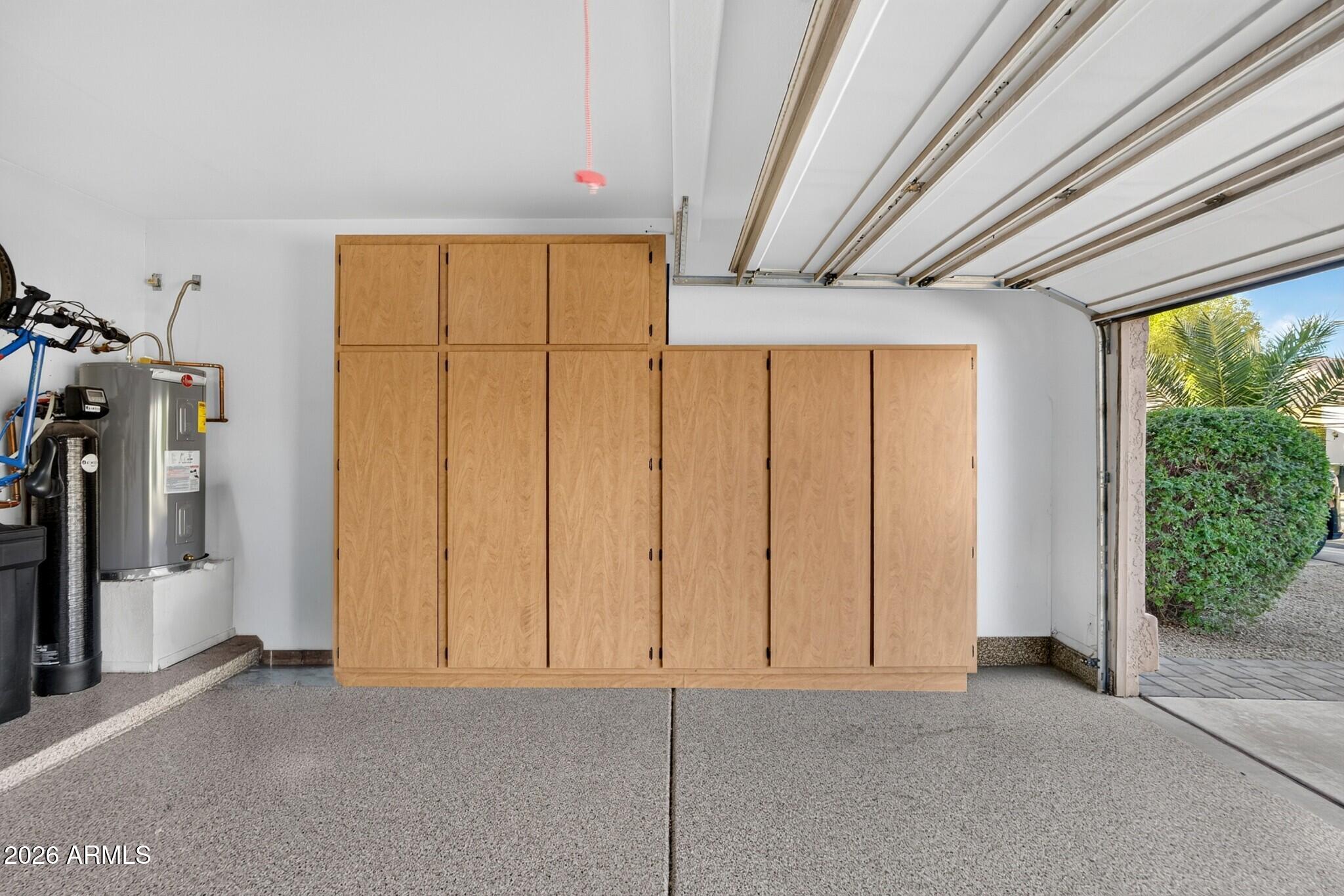 Garage with tall wooden storage cabinets, a water heater, and an open door facing palm trees.