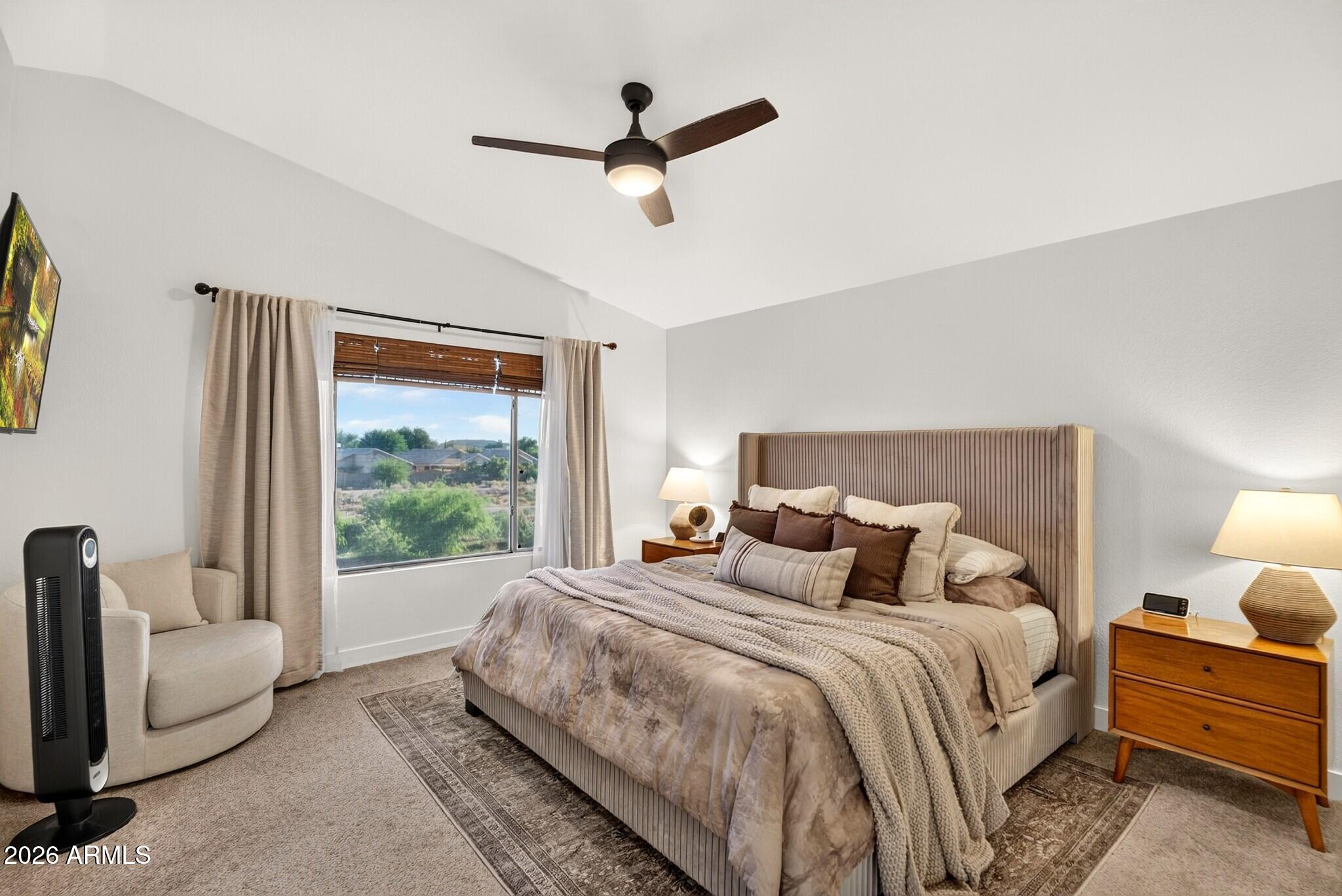 Furnished bedroom with a large upholstered bed, neutral bedding, and a window overlooking greenery.