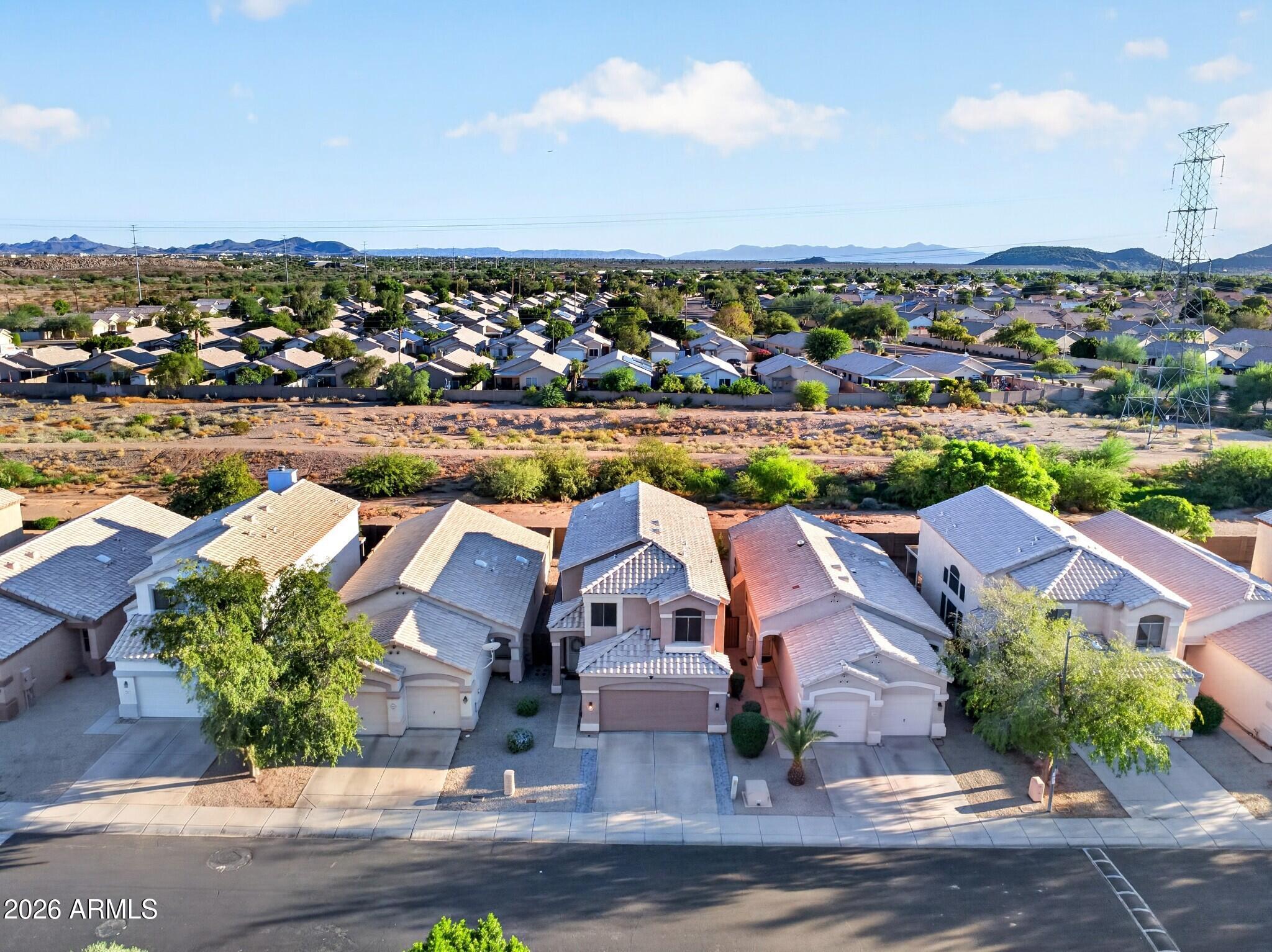 Aerial view of neighborhood homes beside a desert wash, with distant mountains.