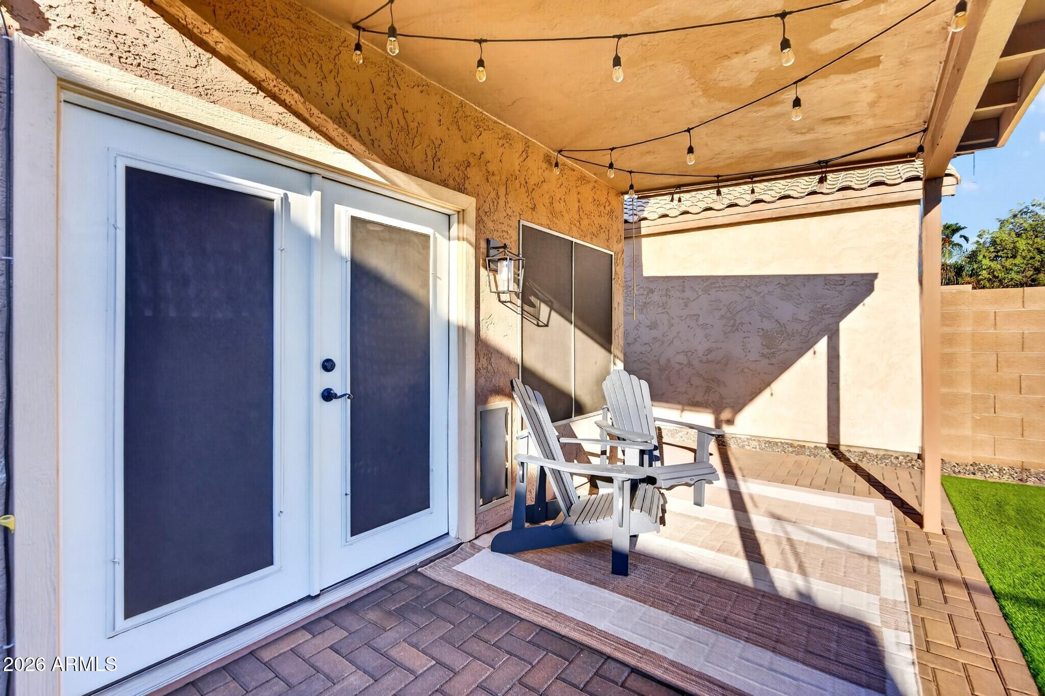 Covered patio with two Adirondack chairs, string lights, screened doors, and paver flooring.